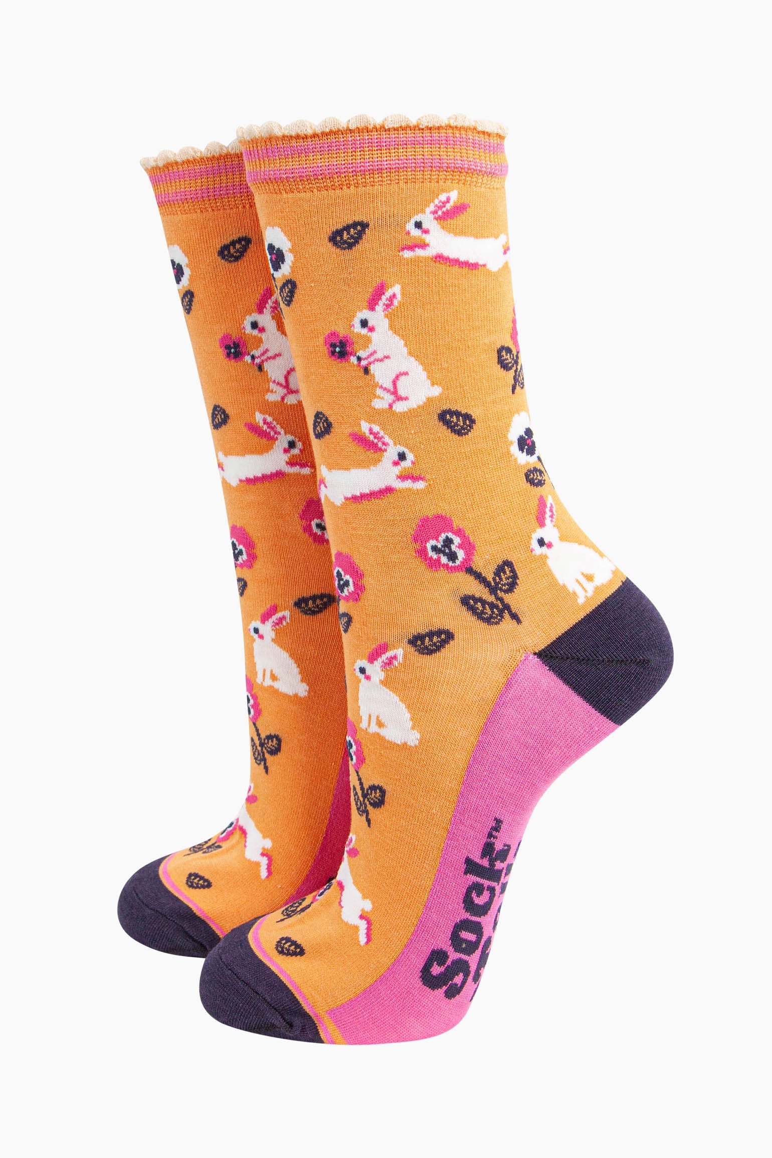 womens bamboo socks orange rabbit and flower. orange bamboo socks with a pattern of white rabbits with pink and white pansy flowers. the toe and heel are contrasting navy blue. the sole is pink with a navy blue sock talk logo visible. 