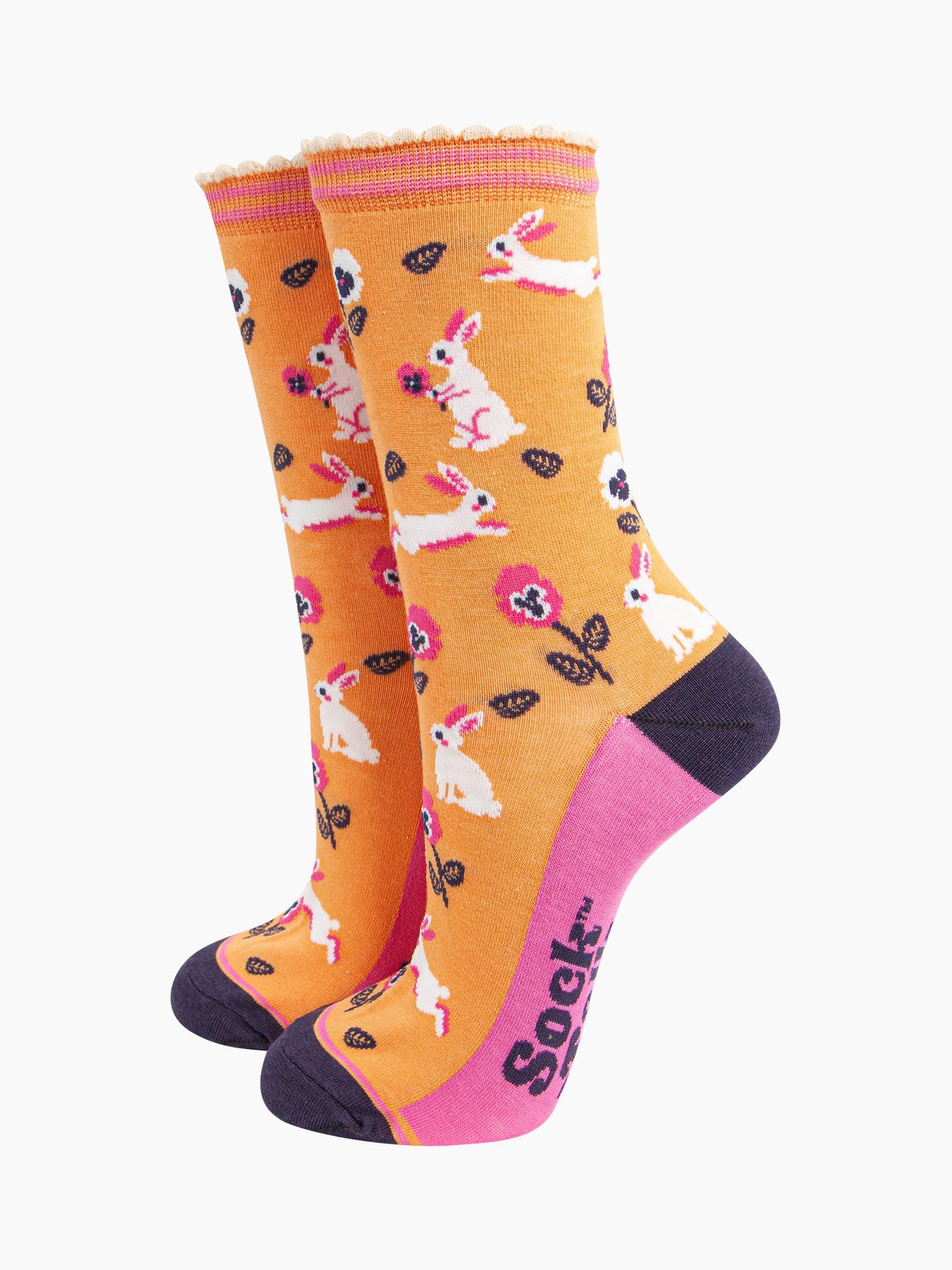 womens bamboo socks orange rabbit and flower. orange bamboo socks with a pattern of white rabbits with pink and white pansy flowers. the toe and heel are contrasting navy blue. the sole is pink with a navy blue sock talk logo visible. 