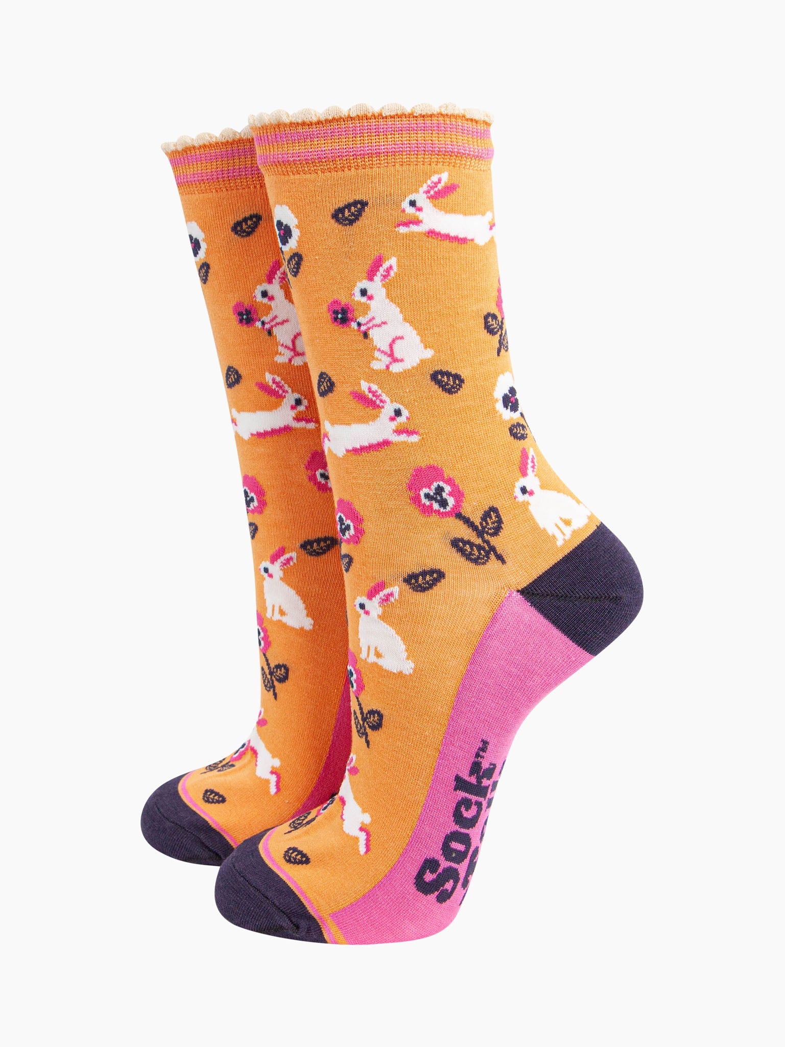 womens bamboo socks orange rabbit and flower. orange bamboo socks with a pattern of white rabbits with pink and white pansy flowers. the toe and heel are contrasting navy blue. the sole is pink with a navy blue sock talk logo visible. 