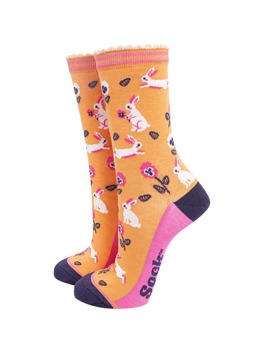 womens bamboo socks orange rabbit and flower. orange bamboo socks with a pattern of white rabbits with pink and white pansy flowers. the toe and heel are contrasting navy blue. the sole is pink with a navy blue sock talk logo visible.