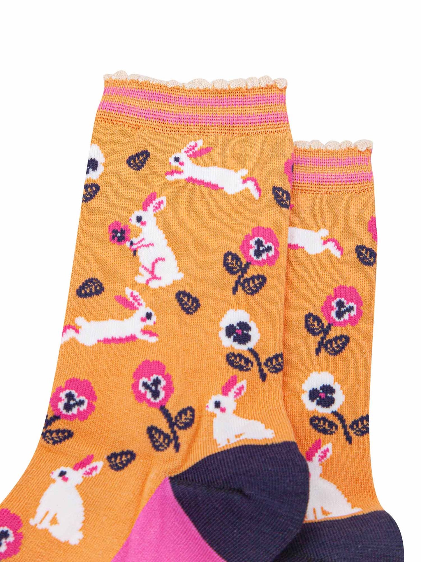 close up of the pattern, the white rabbits are running, sitting and jumping, some are holding flowers. the floral pattern features pink and white pansy like flowers. the cuff is scalloped and has a pastel orange and pink striped pattern.