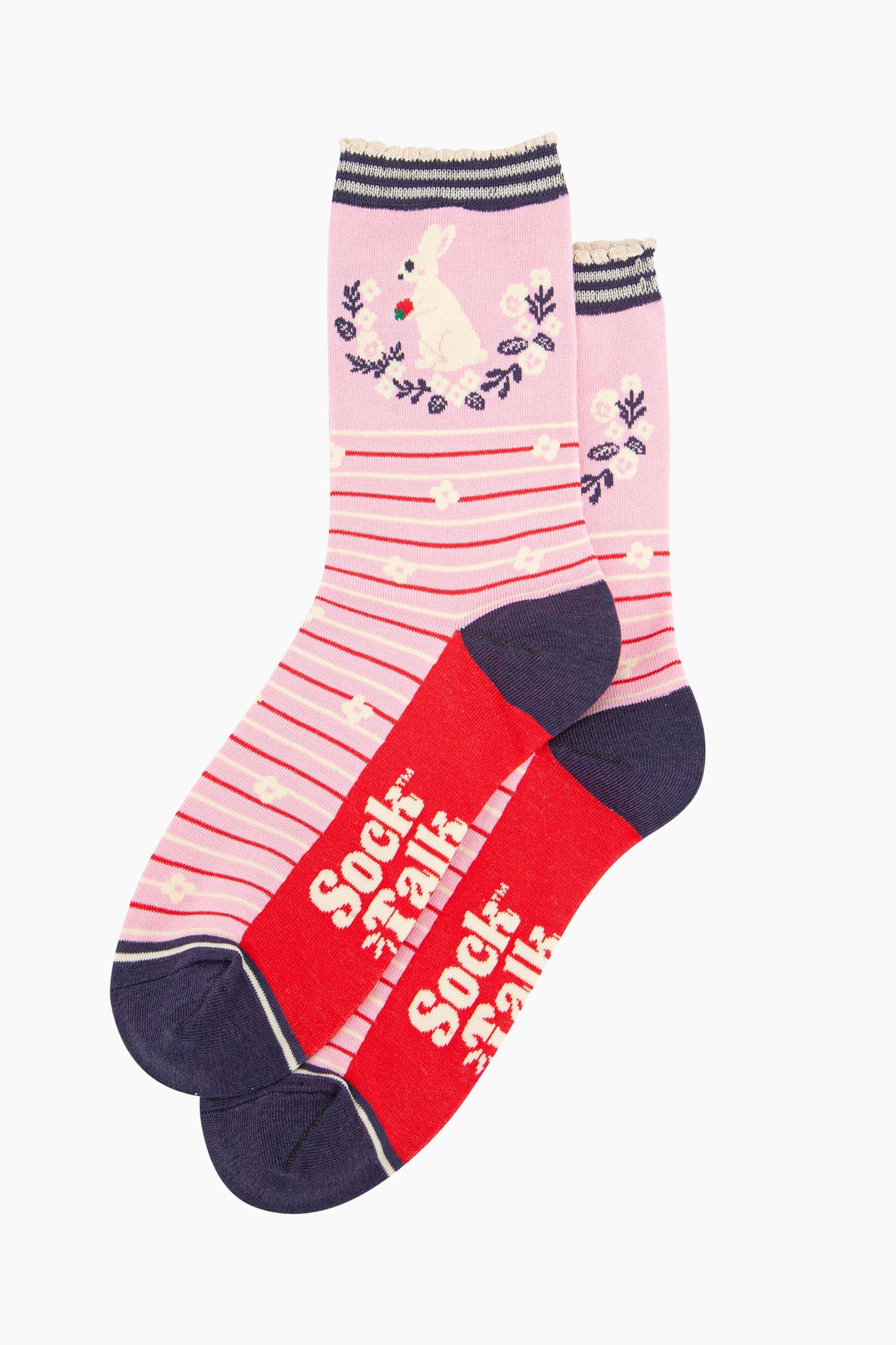 pair of pink rabbit and wreath bamboo socks laying flat, one overlapping the other. showing clearly the pastel pink background of the socks which is contrasted by red and white horizontal pinstripes and white flowers. on the ankle of there is a white rabbit sitting, holding a strawberry in its front paws. the sole of the socks is red, the sock talk logo is shown in cream.