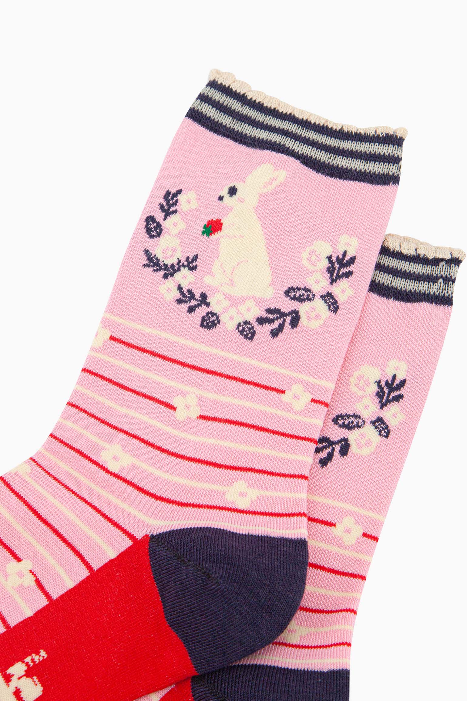 close up of the pattern. on the ankle of the socks is a large white rabbit sitting on its hind legs. it is holding a red strawberry in its paws. underneath the rabbit is a semi circular floral wreath made of white flowers and navy blue leaves. 