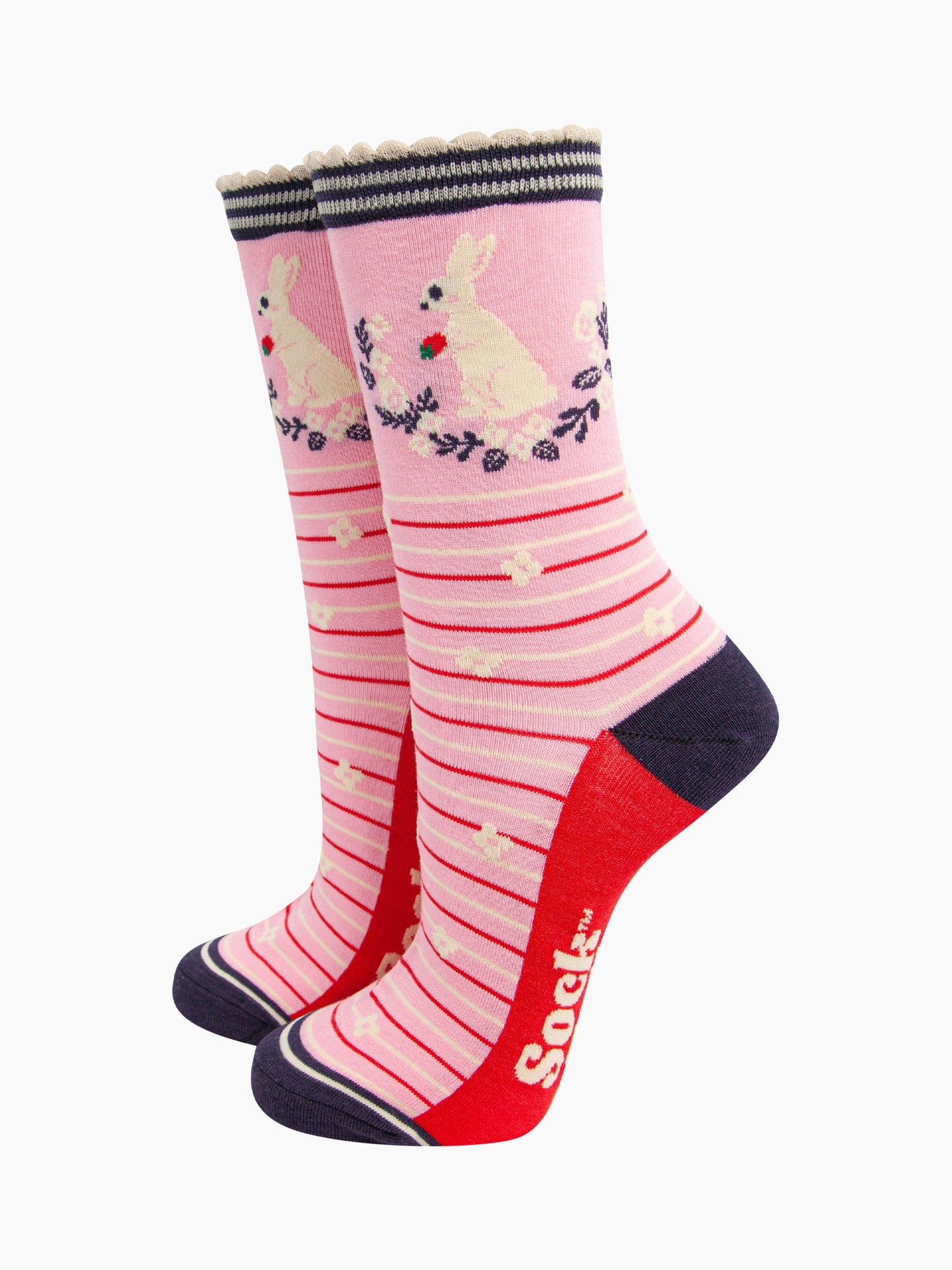 pink rabbit, wreath and strawberry bamboo socks. light pink bamboo socks with red and cream. on the ankle of the socks there is a white rabbit holding a strawberry. the wreath around the rabbit is navy blue and white.