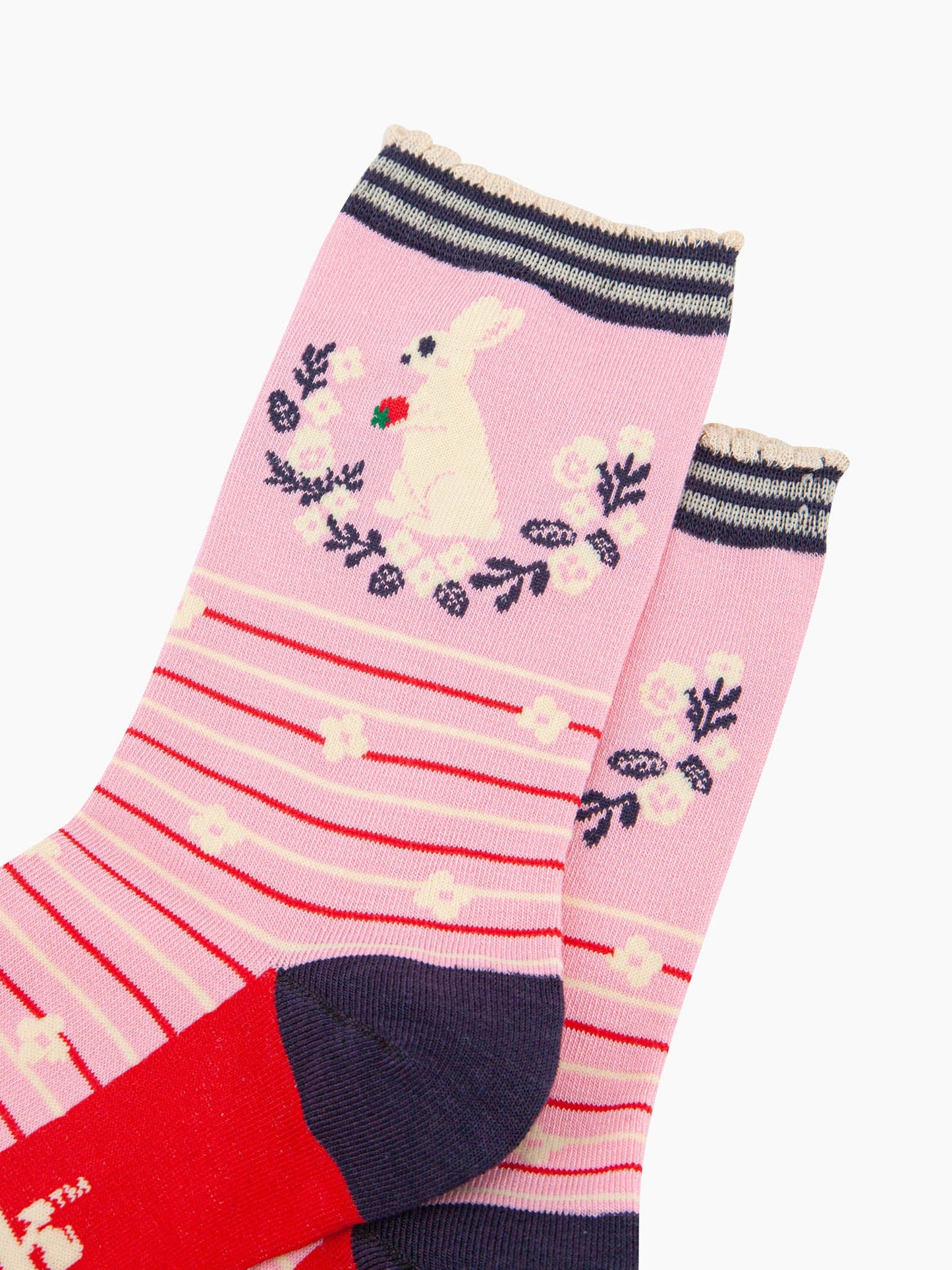 close up of the pattern. on the ankle of the socks is a large white rabbit sitting on its hind legs. it is holding a red strawberry in its paws. underneath the rabbit is a semi circular floral wreath made of white flowers and navy blue leaves. 