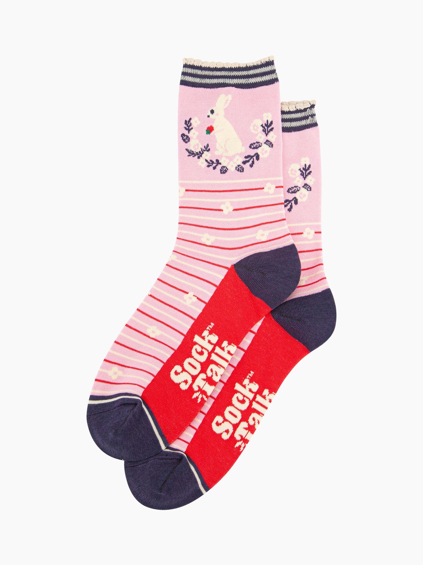 pair of pink rabbit and wreath bamboo socks laying flat, one overlapping the other. showing clearly the pastel pink background of the socks which is contrasted by red and white horizontal pinstripes and white flowers. on the ankle of there is a white rabbit sitting, holding a strawberry in its front paws. the sole of the socks is red, the sock talk logo is shown in cream.