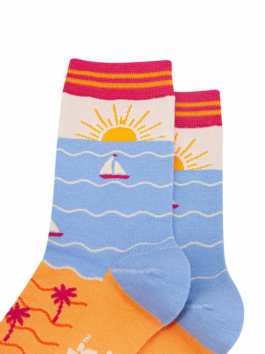 womens-bamboo-socks-cream-blue-beach-sunset-close-up-setting-sun-on-the-ankle-yellow-sandy-beach-blue-ocean-with-sail-boat-depicted-on-the-body-of-the-design
