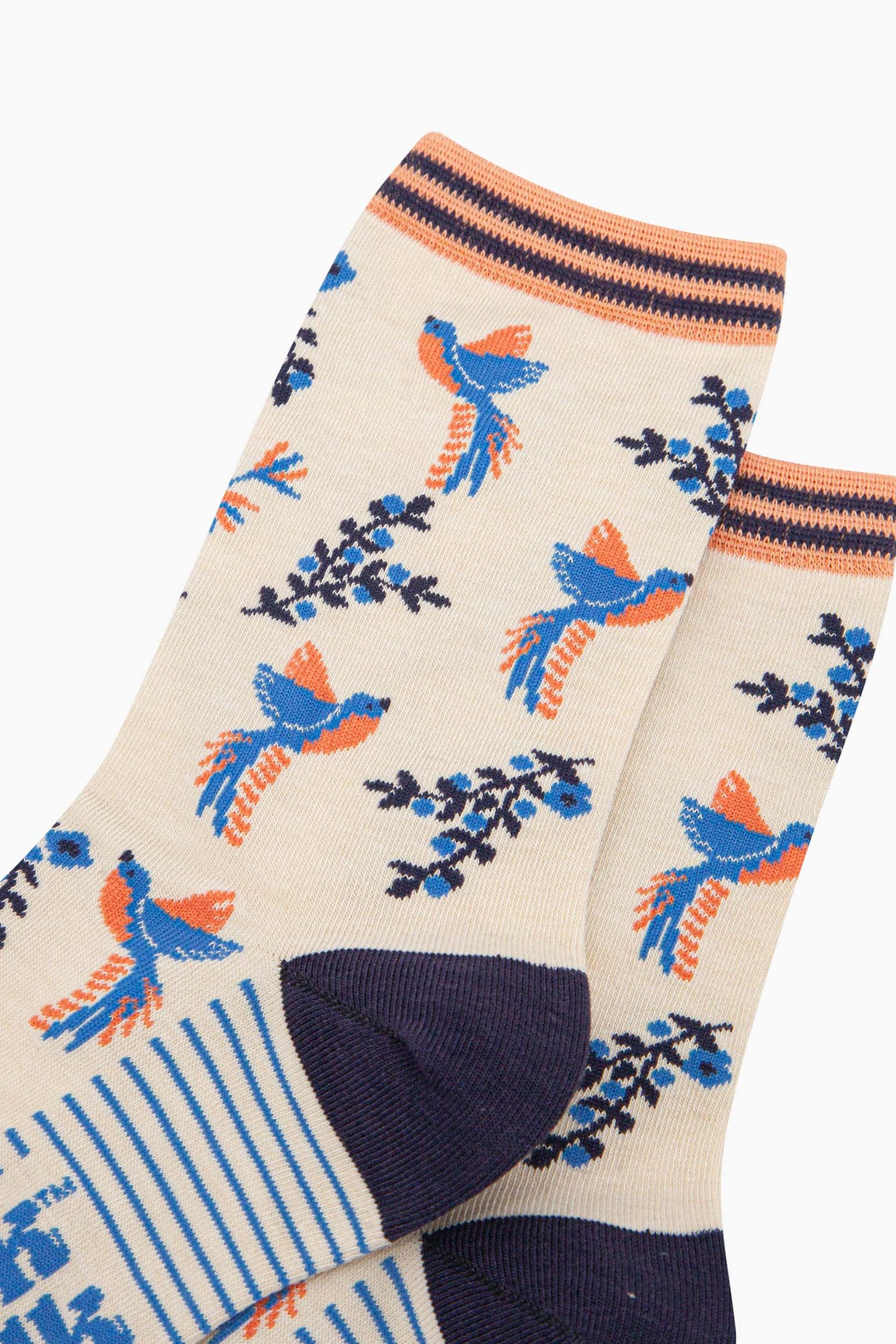 close up of the hummingbird pattern on the cream bamboo socks. the birds are blue with orange bellies. the floral vines are navy blue with light blue flowers. the hummingbirds are shown to be hovering in flight next to the flowers.