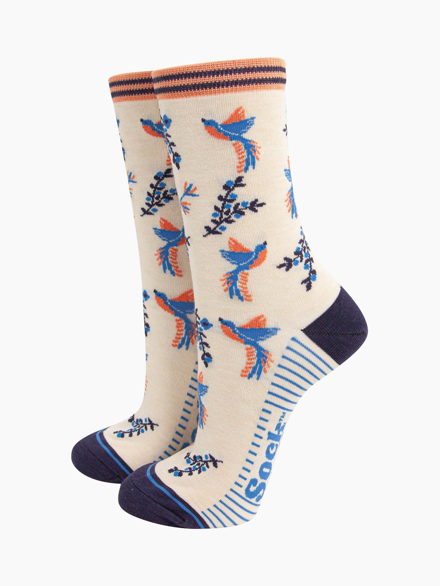 cream hummingbird floral bamboo socks. the hummingbirds and blue and orange and are shown in flight, hovering around floral vines. the toe and heel of the socks are a contrasting navy blue.