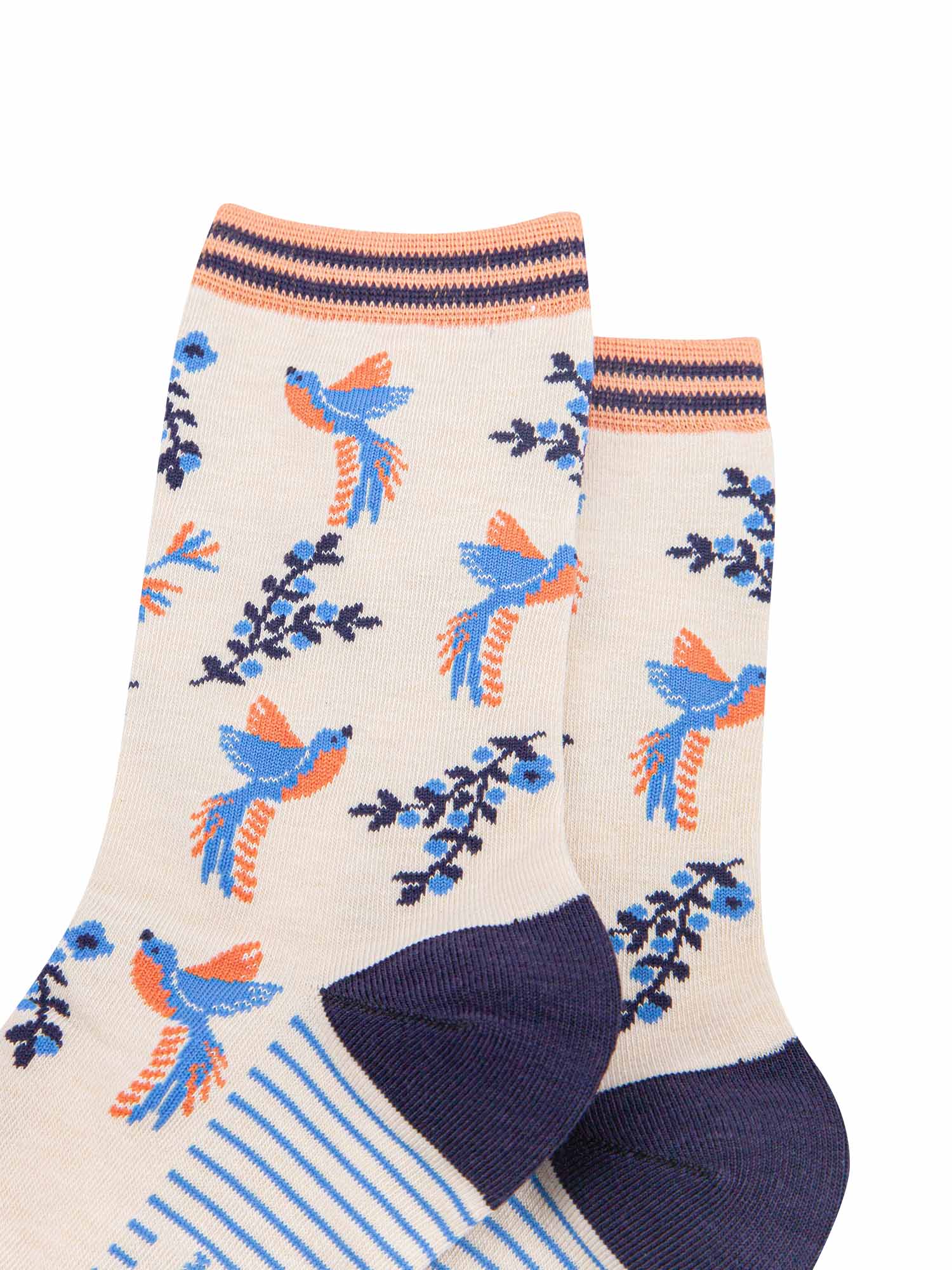 close up of the hummingbird pattern on the cream bamboo socks. the birds are blue with orange bellies. the floral vines are navy blue with light blue flowers. the hummingbirds are shown to be hovering in flight next to the flowers.