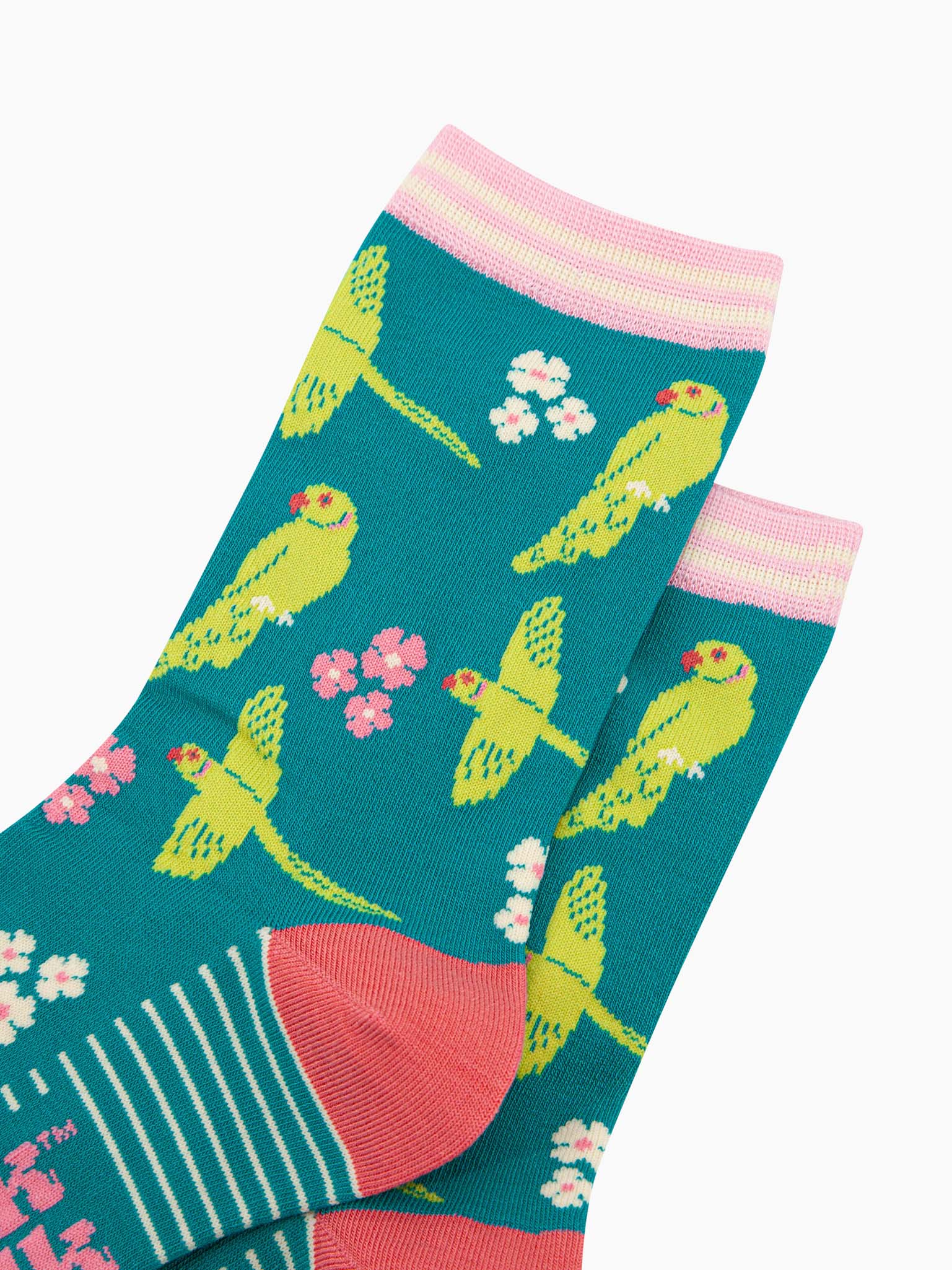 close up of the pattern. the ring necked parakeets are show flying and perching. they are lime green with red eyes and beaks. the ring on the neck is green and pink striped. interspersed among the birds are groups of three flowers in pink and white.