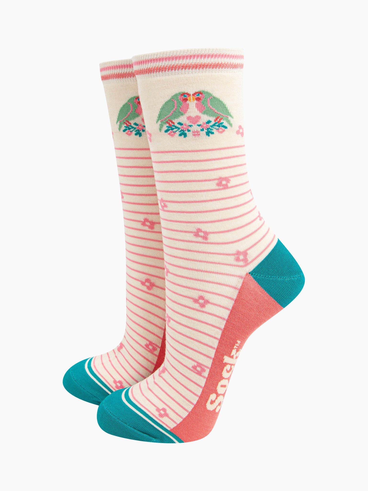 cream lovebird bamboo socks with a pink pinstripe pattern on the body of the socks. the heel and toe and aqua blue, the sole is coral pink. on the ankle of the socks there are a pair of green love birds perched on a floral branch.