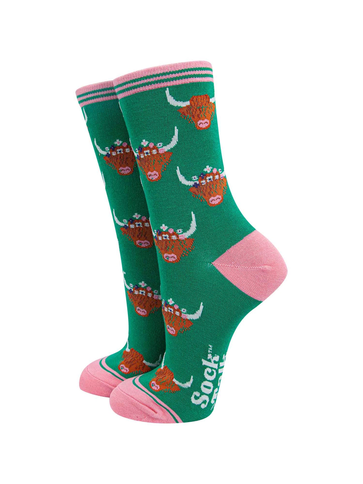green ankle socks with pink toe, heel and cuff featuring a pattern of brown highland cow faces wearing multicoloured floral wreaths