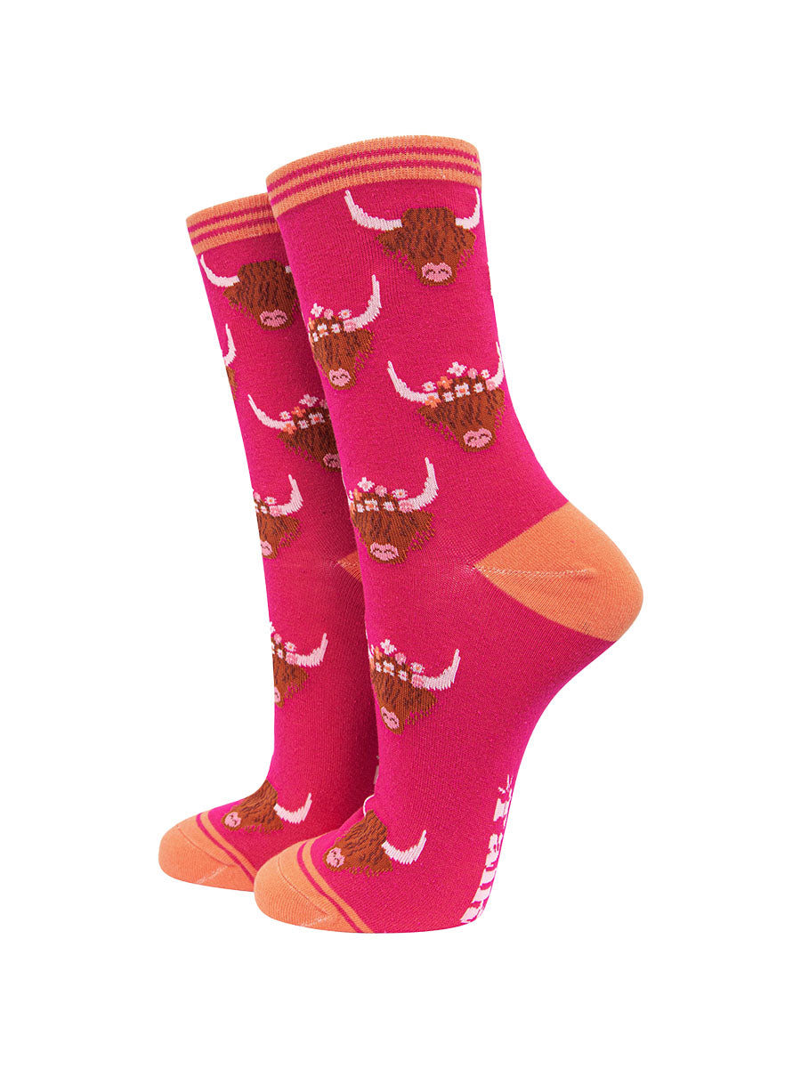 a bright pink ankle sock with a pattern of brown highland cow faces wearing floral crowns all over.