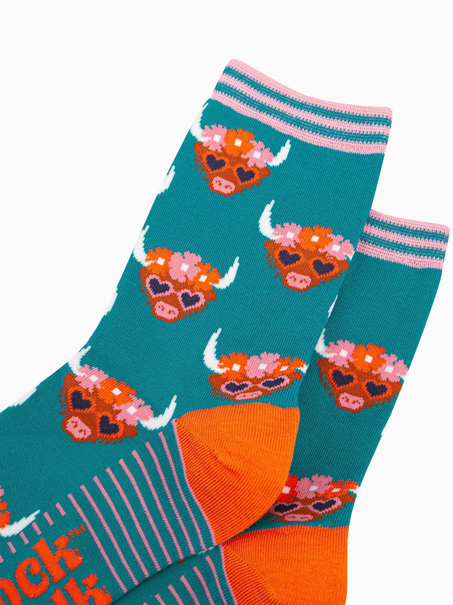 close up of the pattern. the highland cow faces are brown, they have white pointed horns and wear pink love heart sunglasses. on the heads of the cows is a floral wreath composed of pink and orange flowers. the cuff is teal and light pink striped.