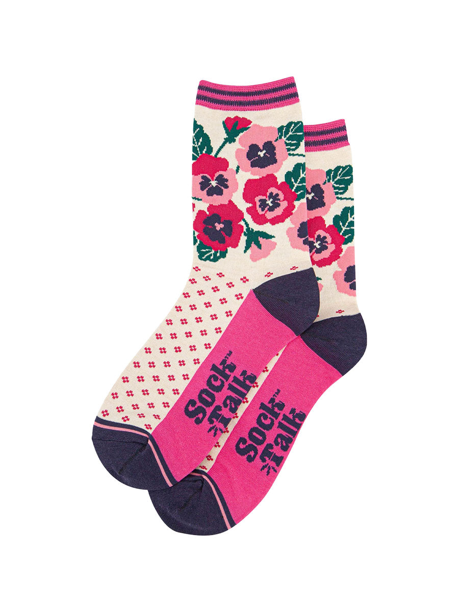 the pair of cream and pink pansy socks laying flat one overlapping the other. showing clearly the cream background of the socks which is contrasted by a fuchsia pink dotted pattern. on the ankle of the socks there is an arrangement of pink and fuchsia pansies. the sock talk logo is navy blue visible on the base of the sole