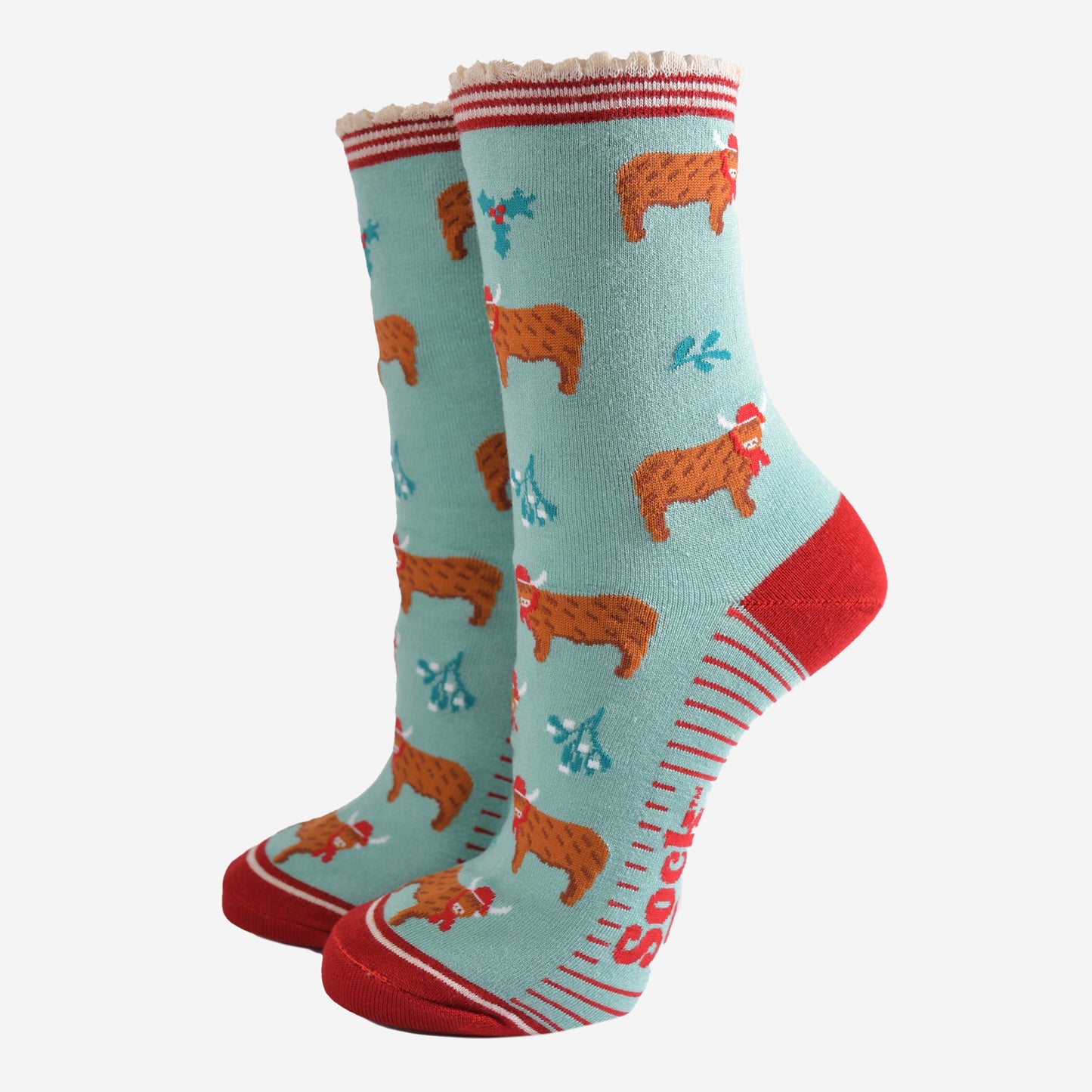 mint green bamboo socks with a red striped scalloped cuff and an all over pattern of highland cows wearing santa hats, the socks are further decorated with holly and mistletoe accents