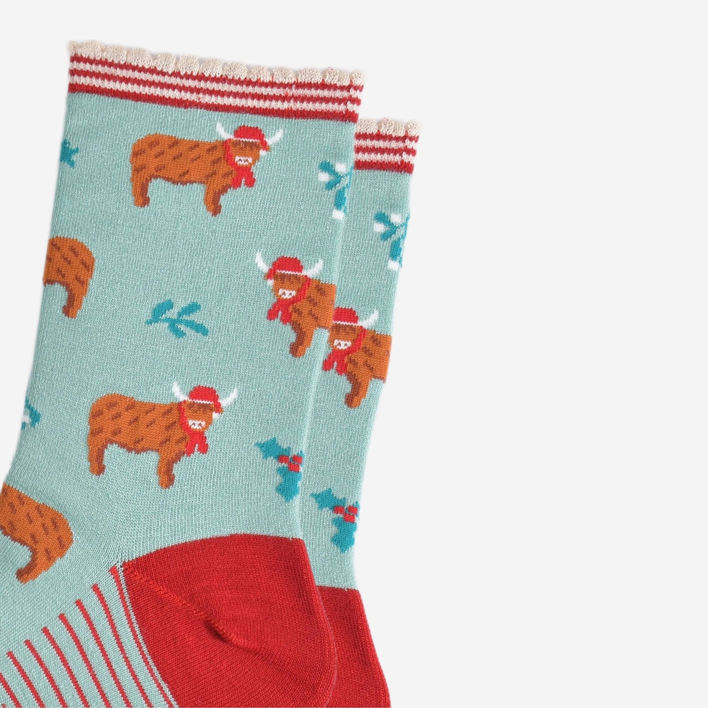 close up of the highland cow pattern on the socks, the cows are wearing red santa hats and red scarves, there are sprigs of holly and mistletoe throughout the design