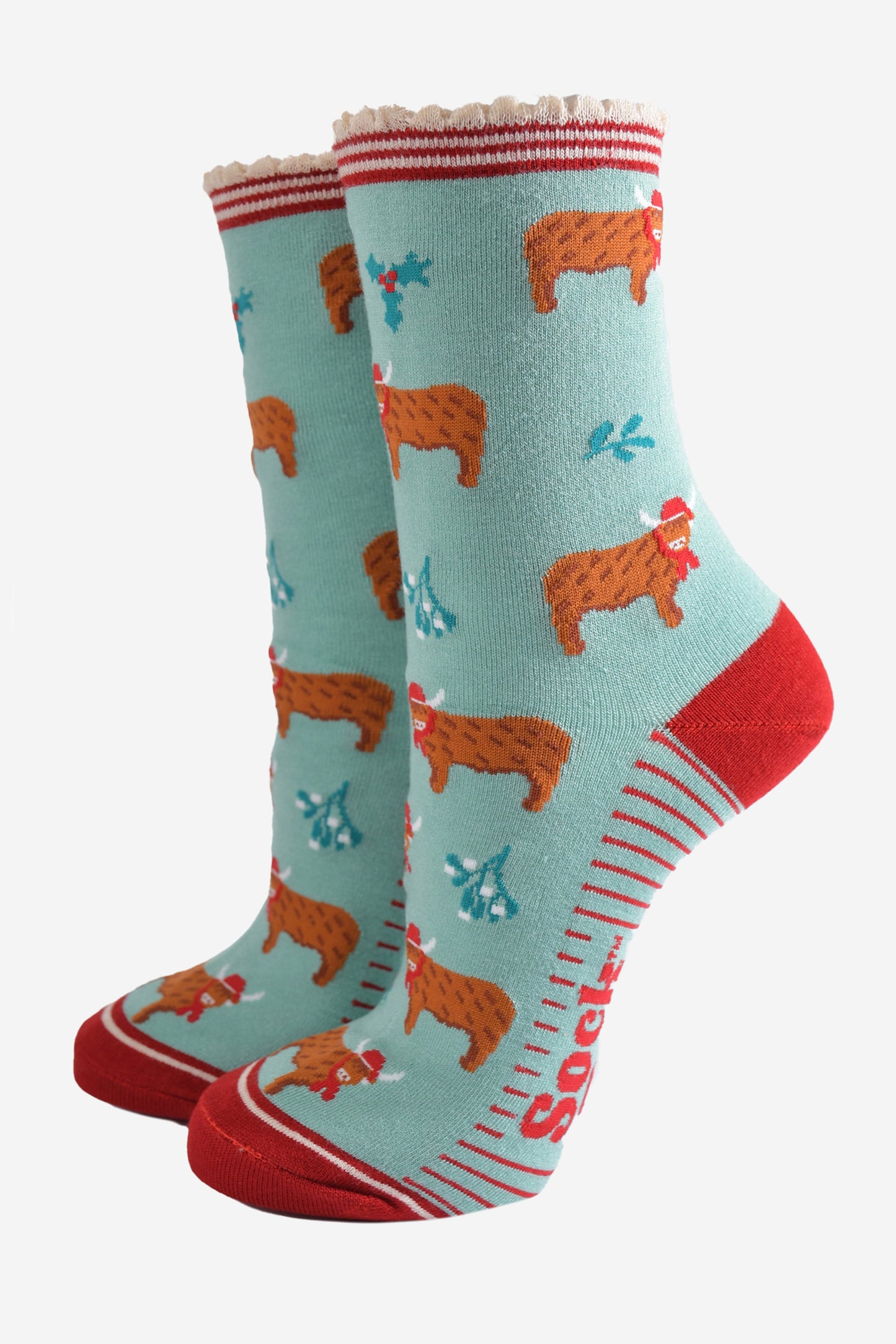 mint green bamboo socks with a red striped scalloped cuff and an all over pattern of highland cows wearing santa hats, the socks are further decorated with holly and mistletoe accents