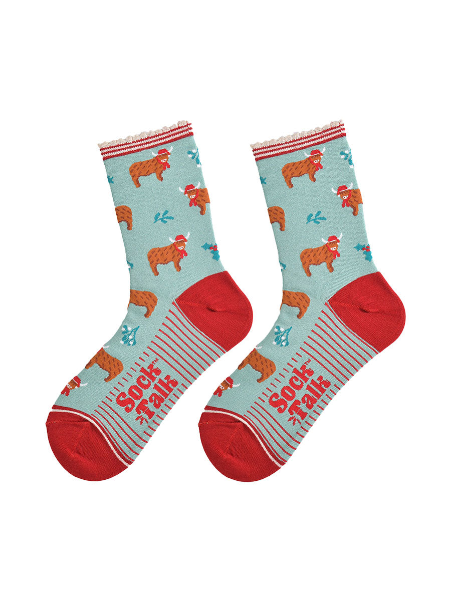 christmas highland cow socks laying flat, showing the all over cow pattern, mistletoe and holly accents, the sole has a red pinstripe design