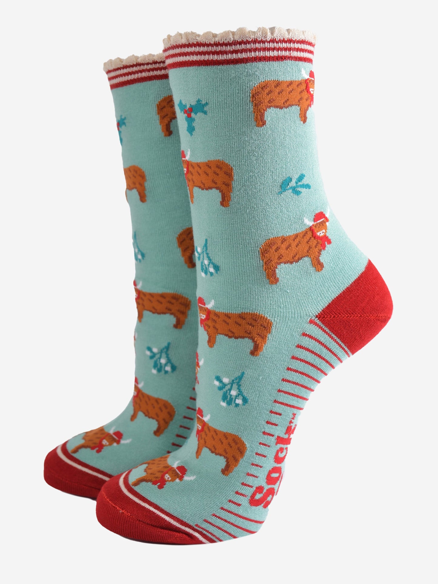 mint green bamboo socks with a red striped scalloped cuff and an all over pattern of highland cows wearing santa hats, the socks are further decorated with holly and mistletoe accents