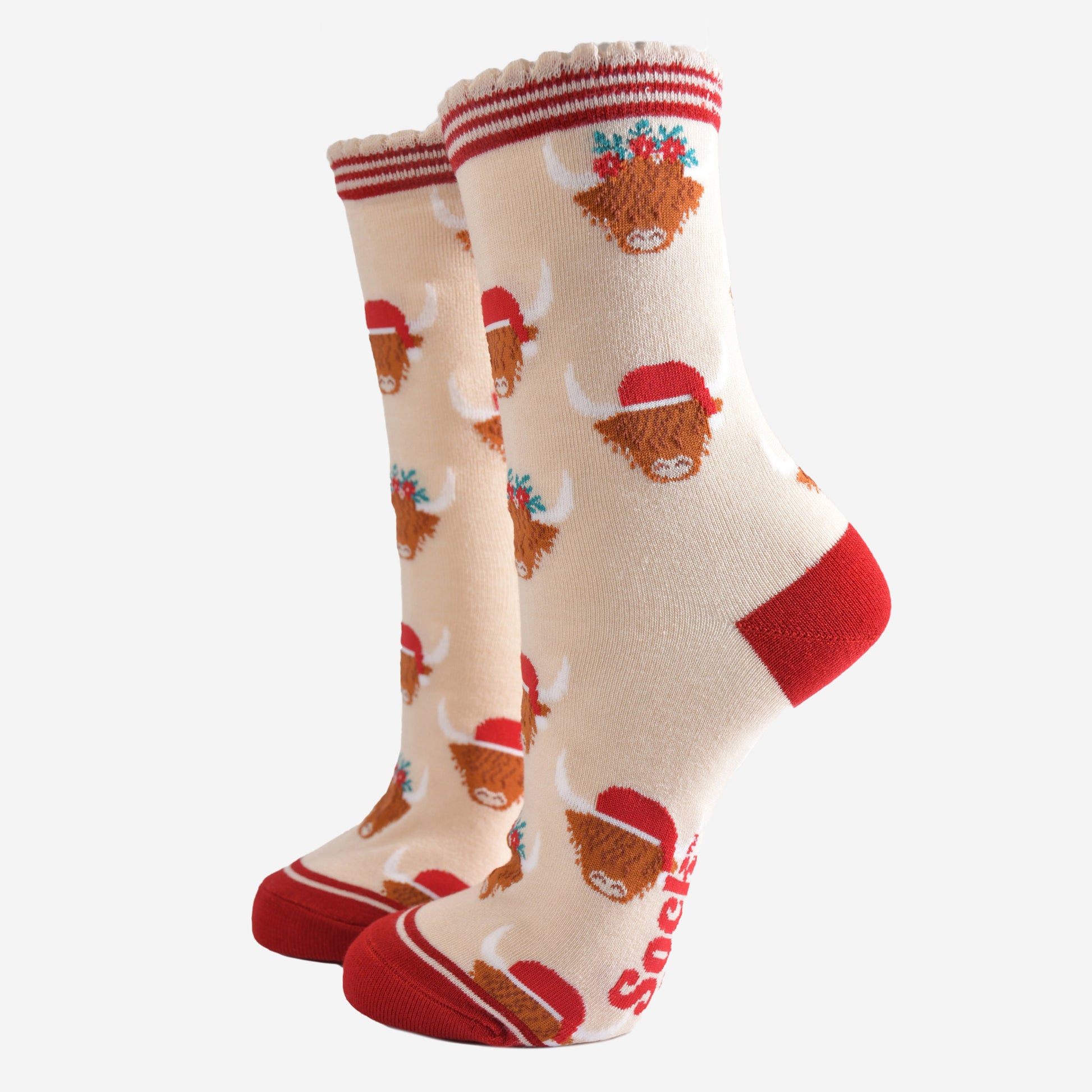 cream socks with red heel, toe and striped cuff featuring a pattern of highland cows wearing santa hats and floral crowns