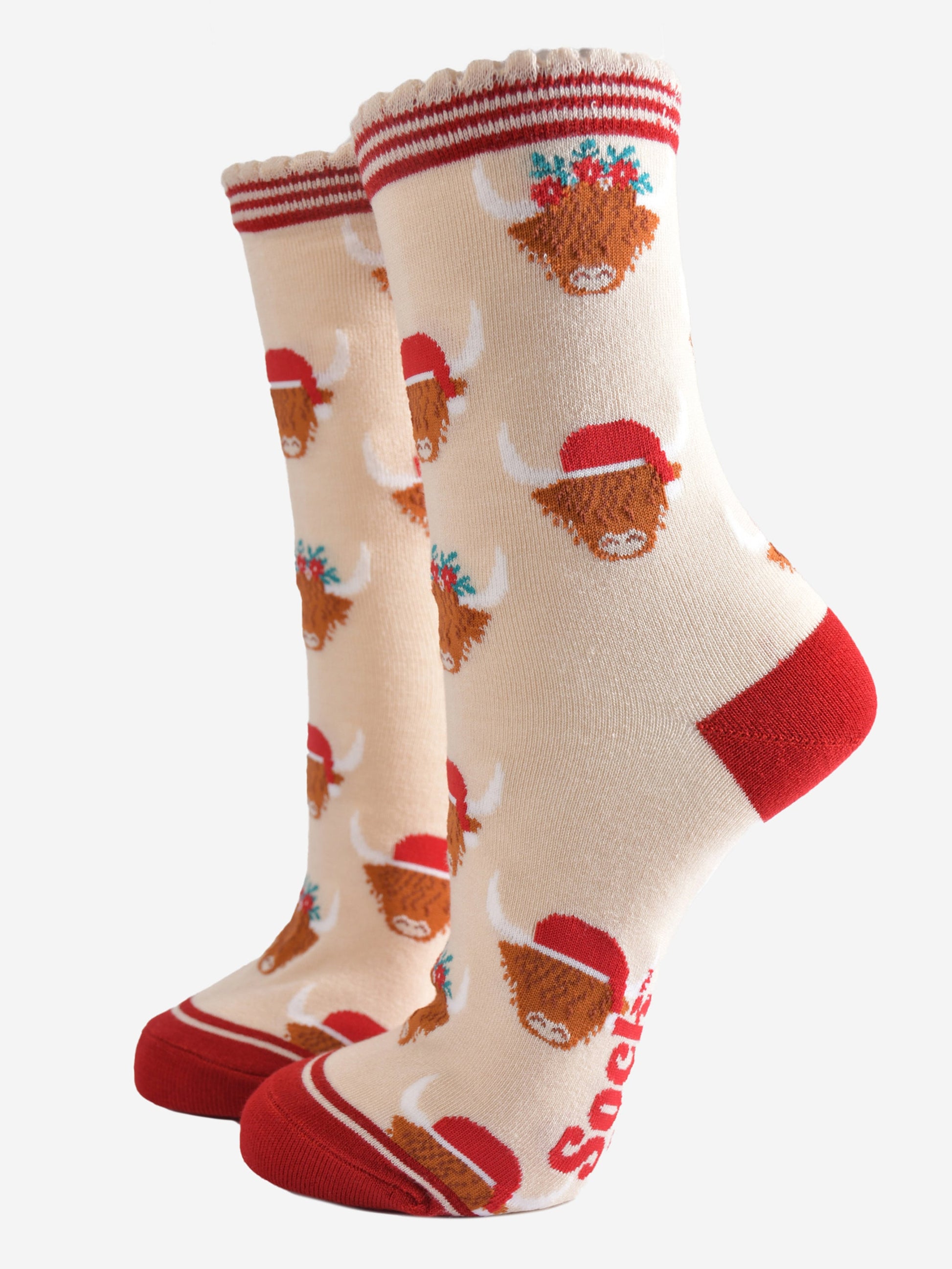 cream socks with red heel, toe and striped cuff featuring a pattern of highland cows wearing santa hats and floral crowns