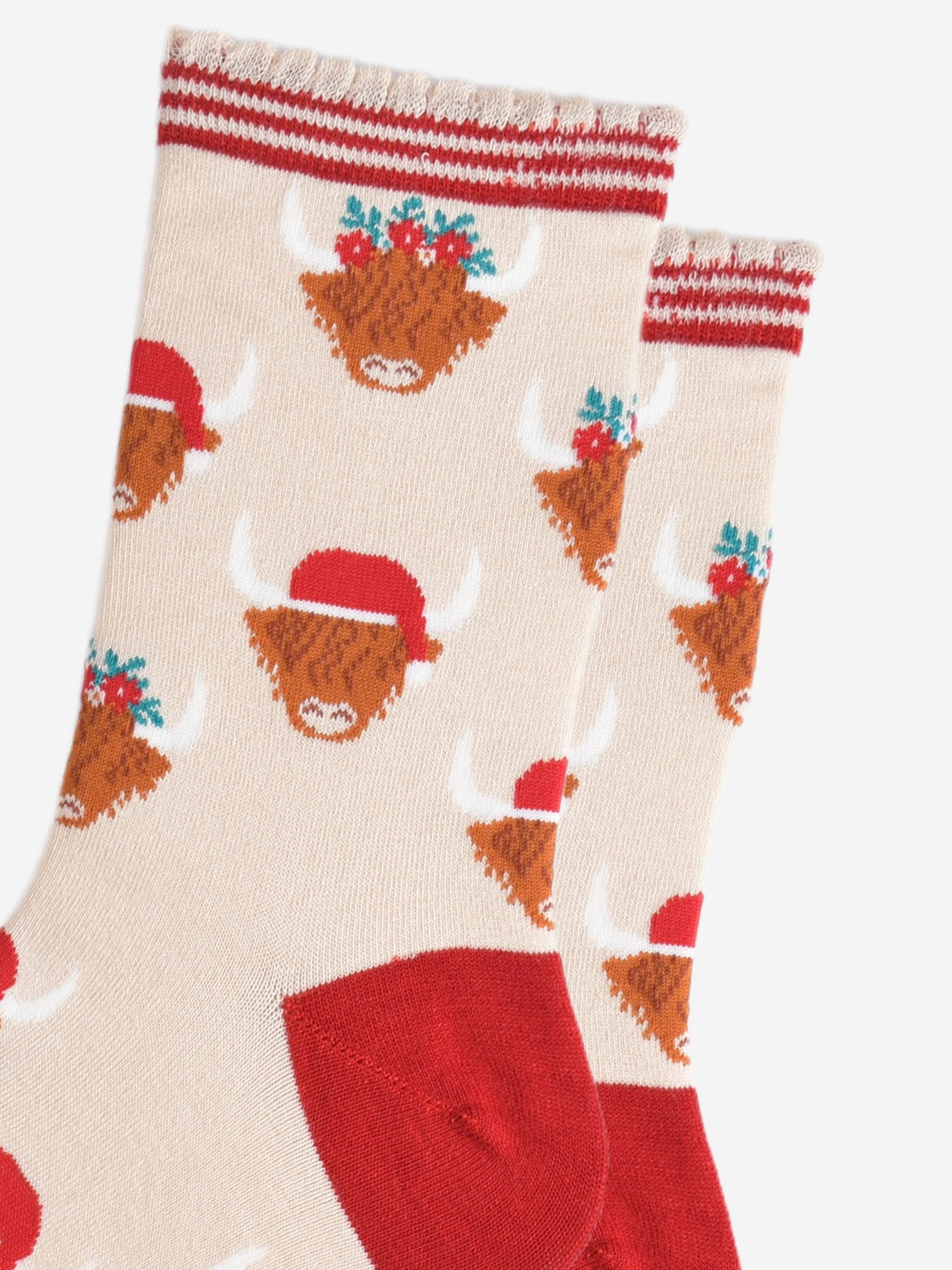 close up of the highland cow pattern on the socks, there are two designs, one with the cow wearing a red santa hat, the other the cow is wearing a festive green and red floral wreath as a crown