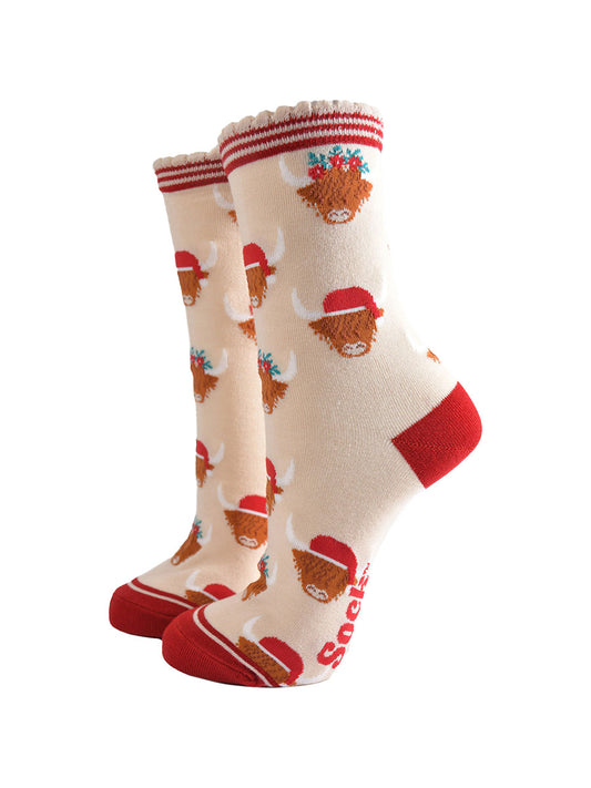 cream socks with red heel, toe and striped cuff featuring a pattern of highland cows wearing santa hats and floral crowns

