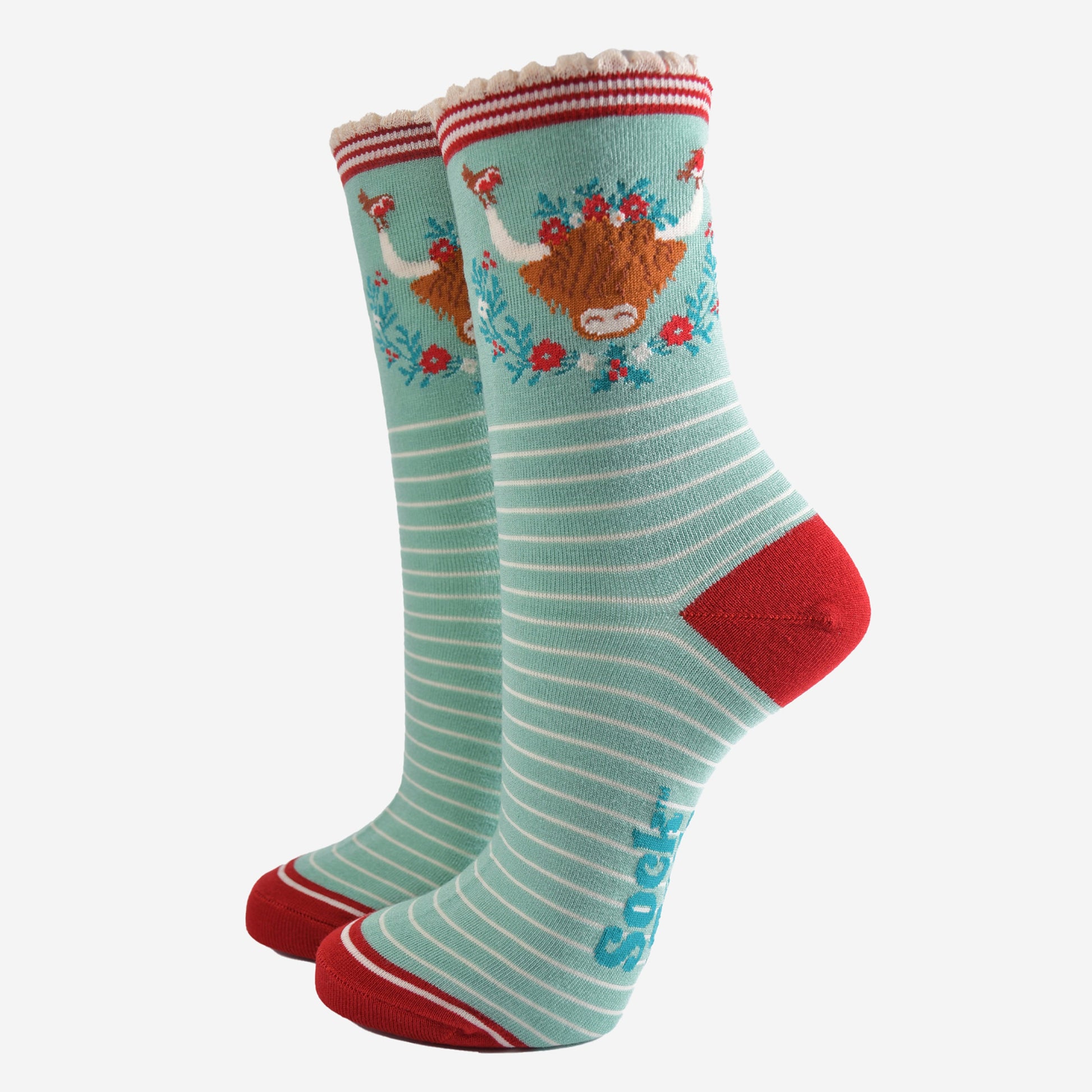mint green bamboo socks with a large highland cow on the ankle, the highland cow is surrounded by red robin birds, and holly, the socks have a scalloped edge and a white pinstripe