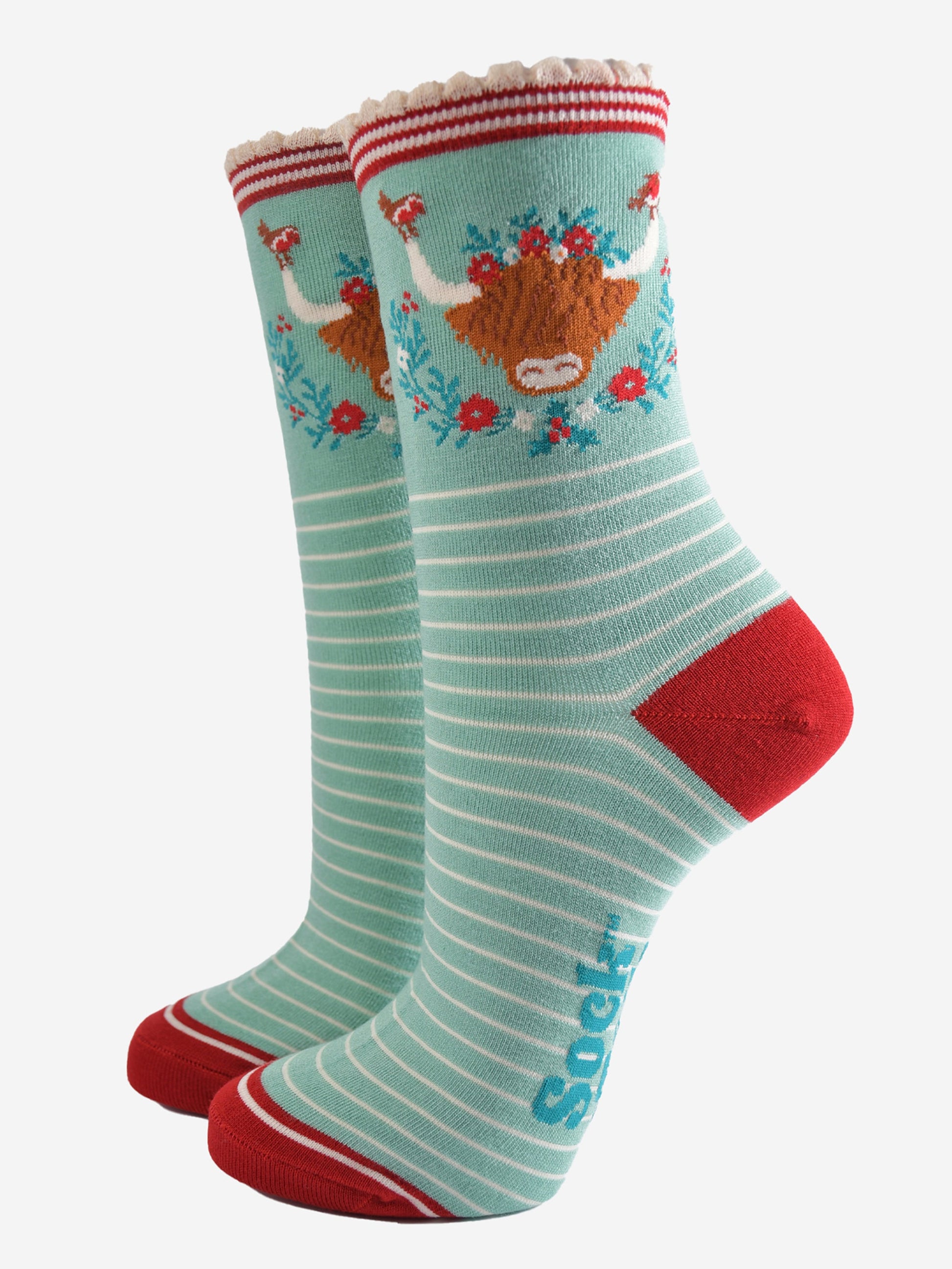 mint green bamboo socks with a large highland cow on the ankle, the highland cow is surrounded by red robin birds, and holly, the socks have a scalloped edge and a white pinstripe