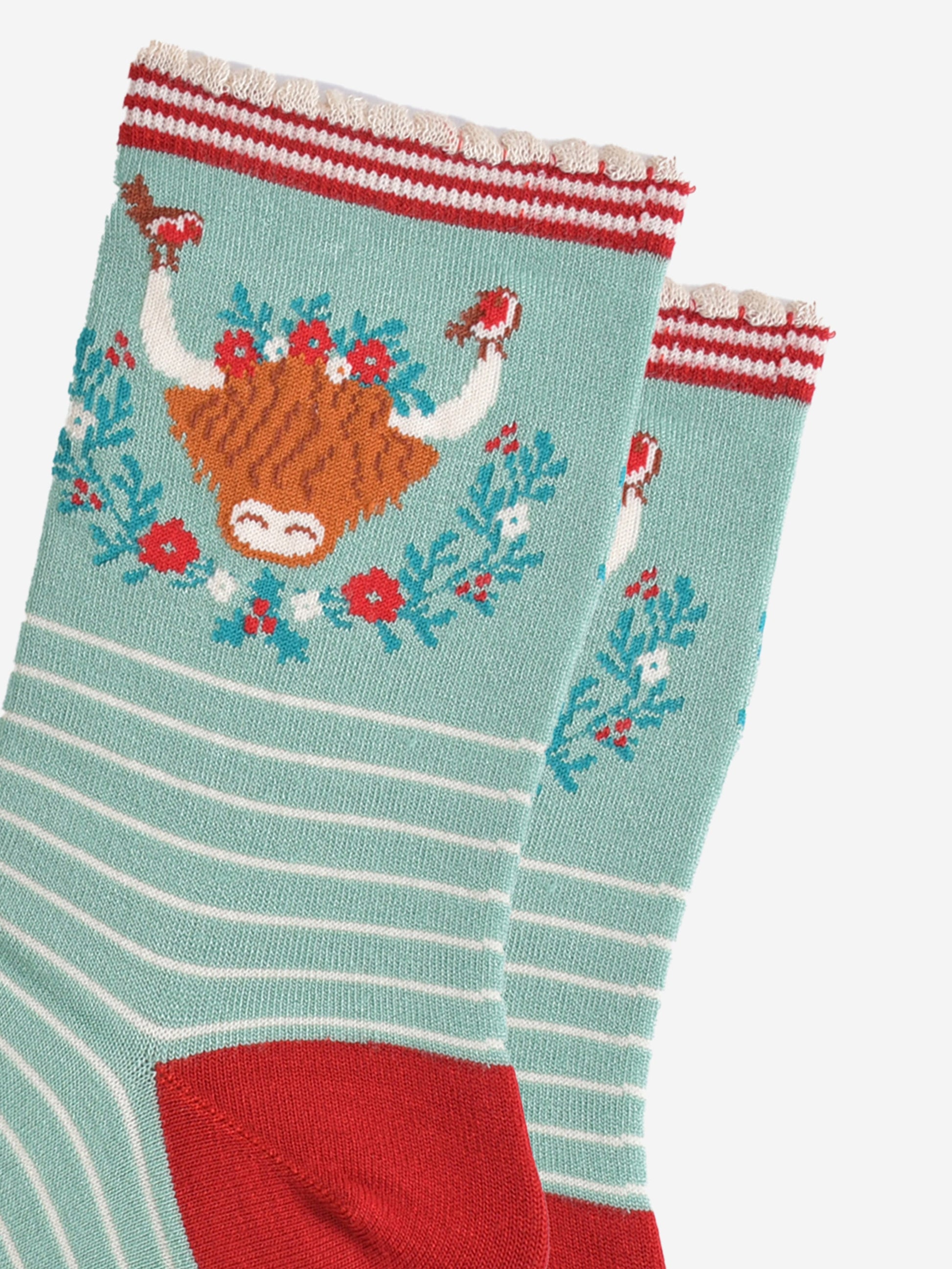 close up of the highland cow design on the ankle of the socks, there are robins perched on the tips of the horns, the wreath is green, red and yellow floral design