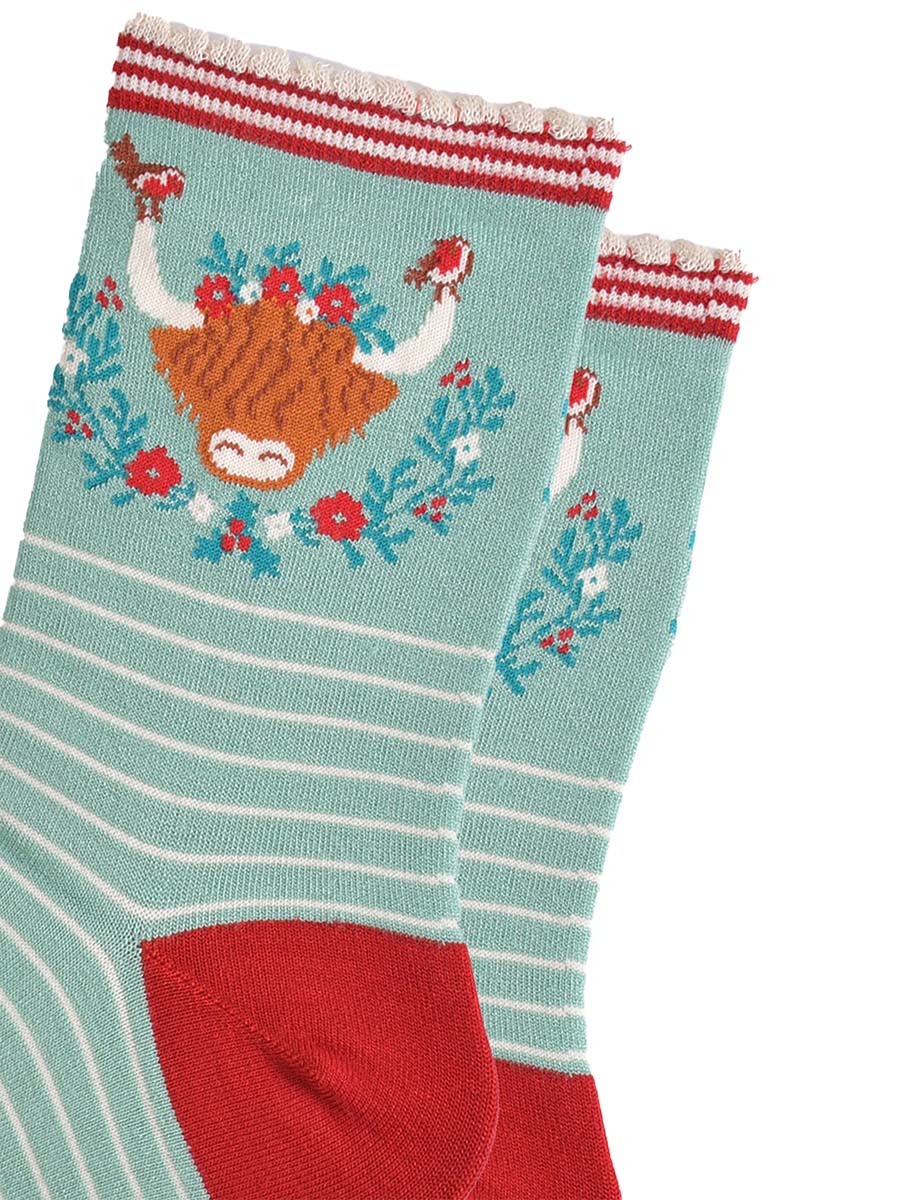 close up of the highland cow design on the ankle of the socks, there are robins perched on the tips of the horns, the wreath is green, red and yellow floral design