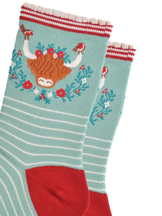 close up of the highland cow design on the ankle of the socks, there are robins perched on the tips of the horns, the wreath is green, red and yellow floral design
