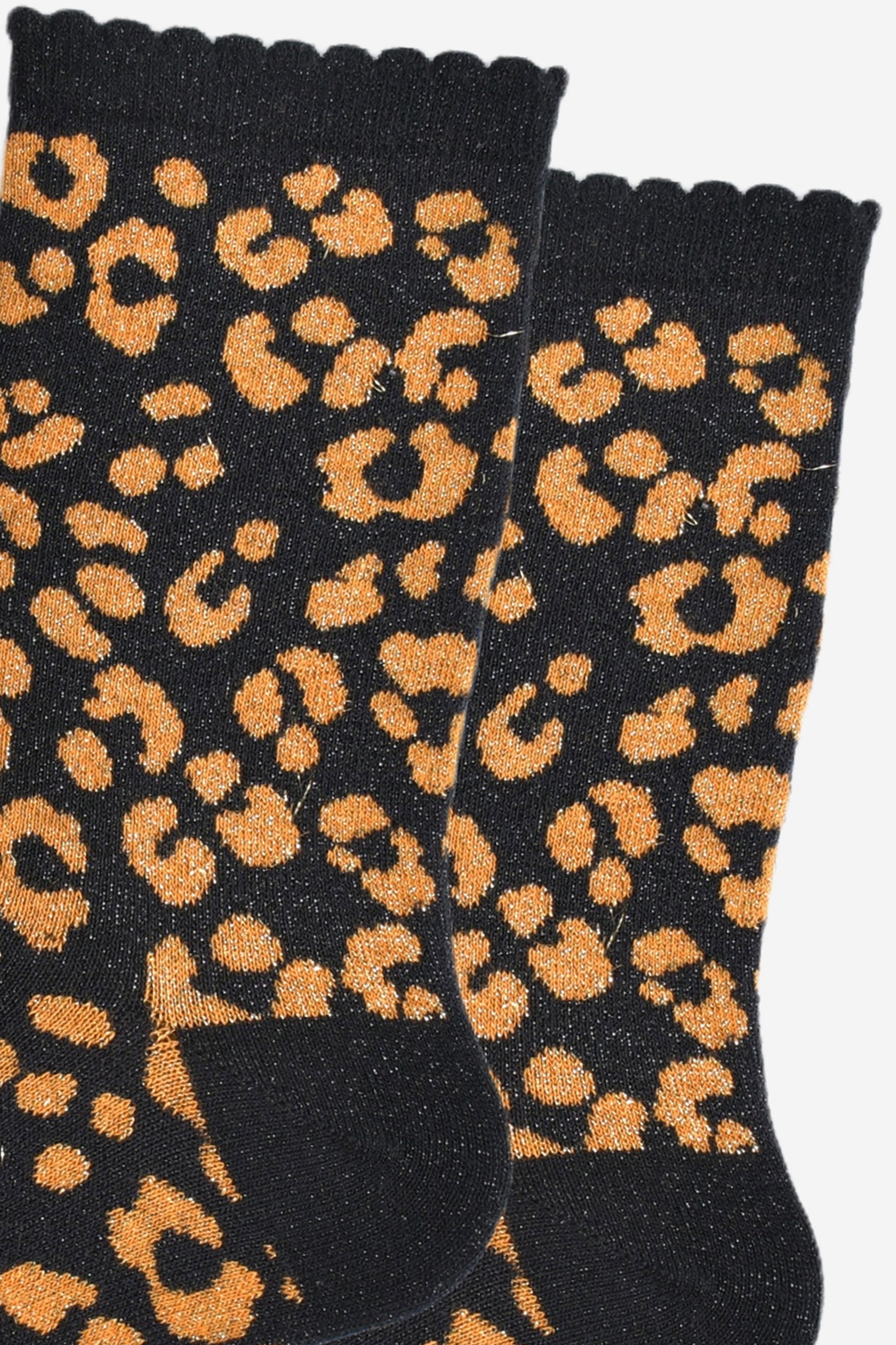 close up of the orange leopard print pattern on the socks, there is a visible silver glitter sparkle all over the design. the pink print contrasts with the black base of the socks