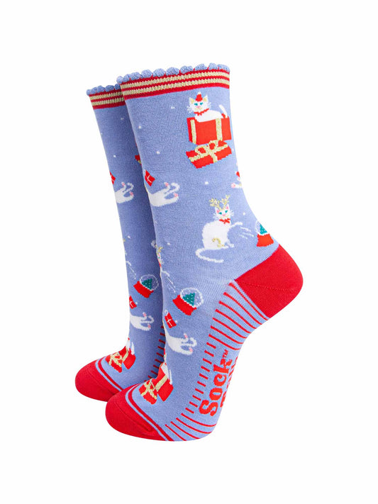 light blue socks with a contrasting red heel, toe and striped cuff and sole with a pattern of white cats playing with snow globes and christmas presents