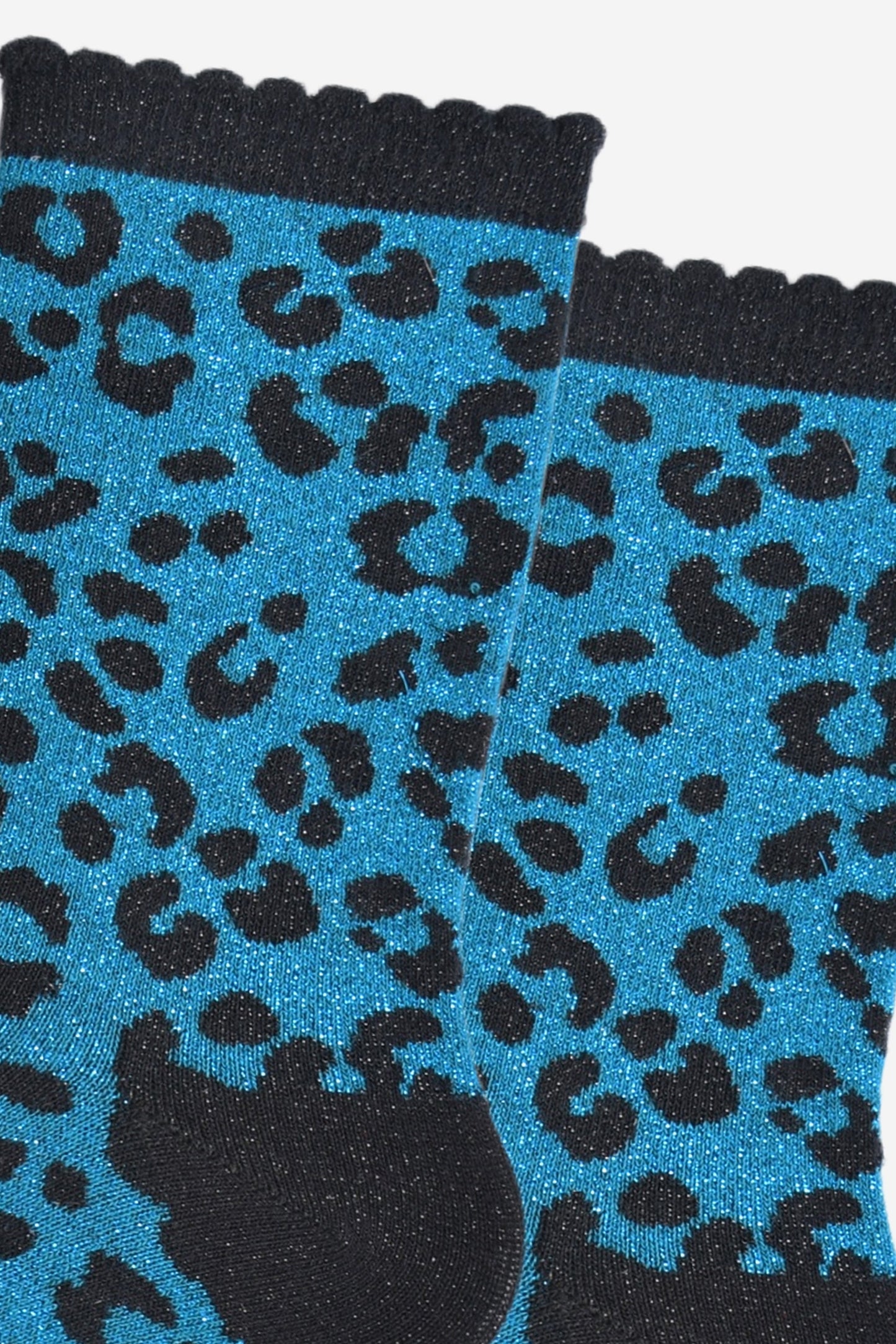 close up of the teal leopard print pattern on the socks, there is a visible silver glitter sparkle all over the design. the teal blue print contrasts with the black base of the socks