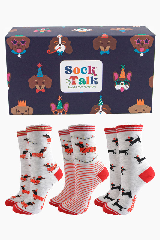 three pairs of grey and red festive sausage dog socks with a navy blue gift box featuring dogs wearing party hats and novelty sunglasses