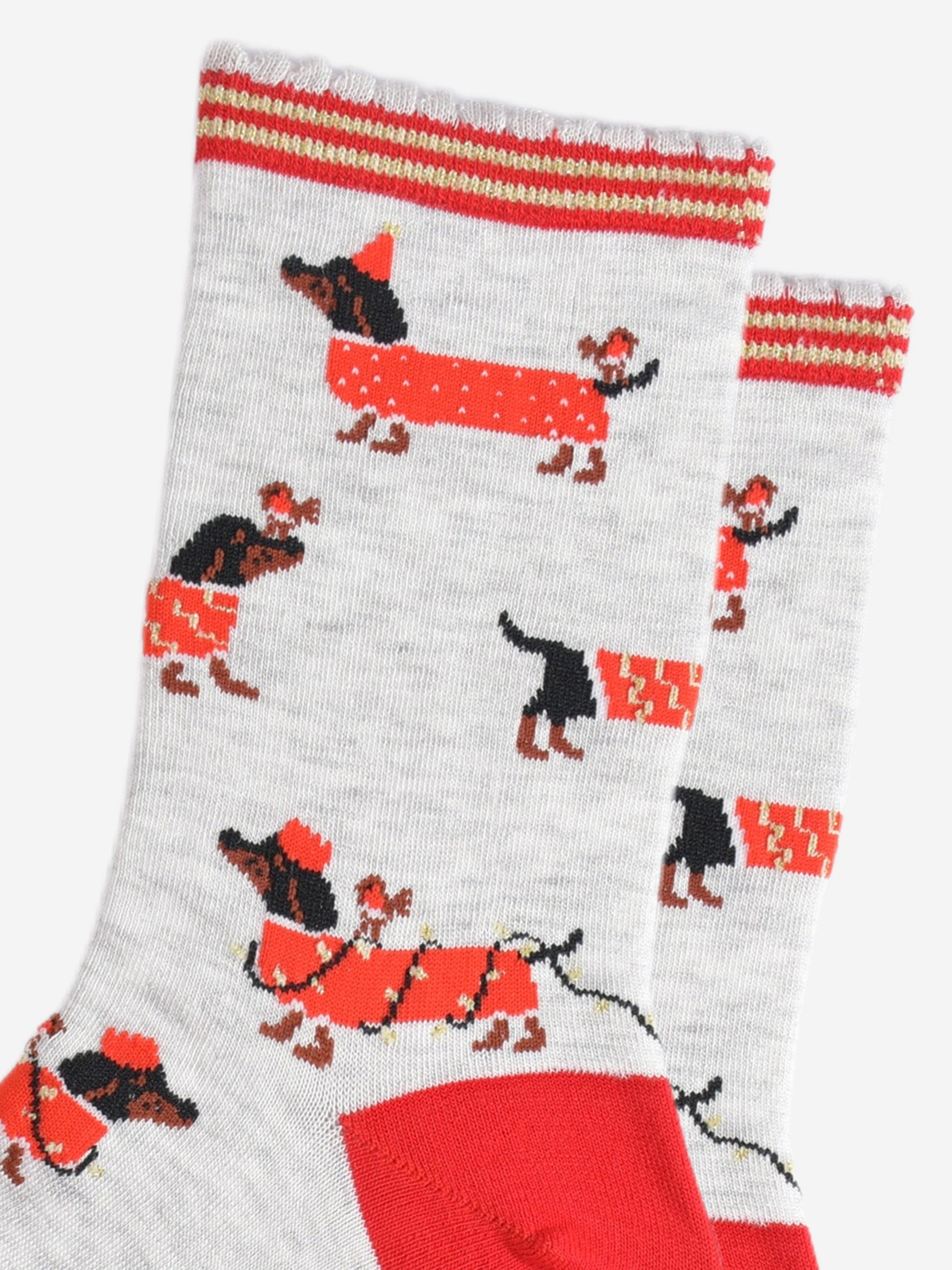 close up of the sausage dog pattern, the dogs are black and wearing red coats. one dog is wearing a red party hat and has a robin on its back. one dog is wrapped in gold party lights and is wearing a red party crown, also with a robin on its back. the last design is a dog wearing a red and gold coat and has a robin sitting on its nose.