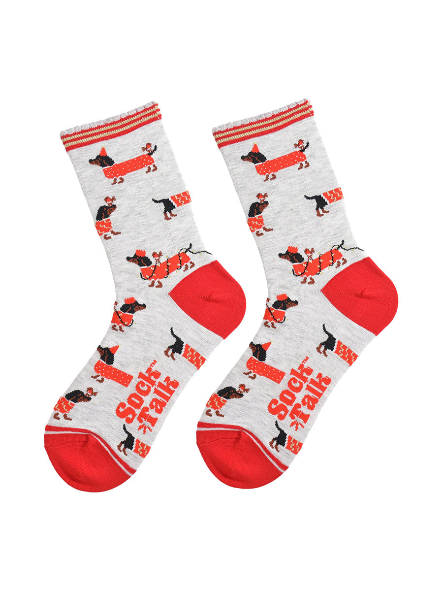 showing the socks laying flat, there is an all over pattern of black sausage dogs wearing red festive coats, party lights and hats. there are also red robins playing with the sausage dogs