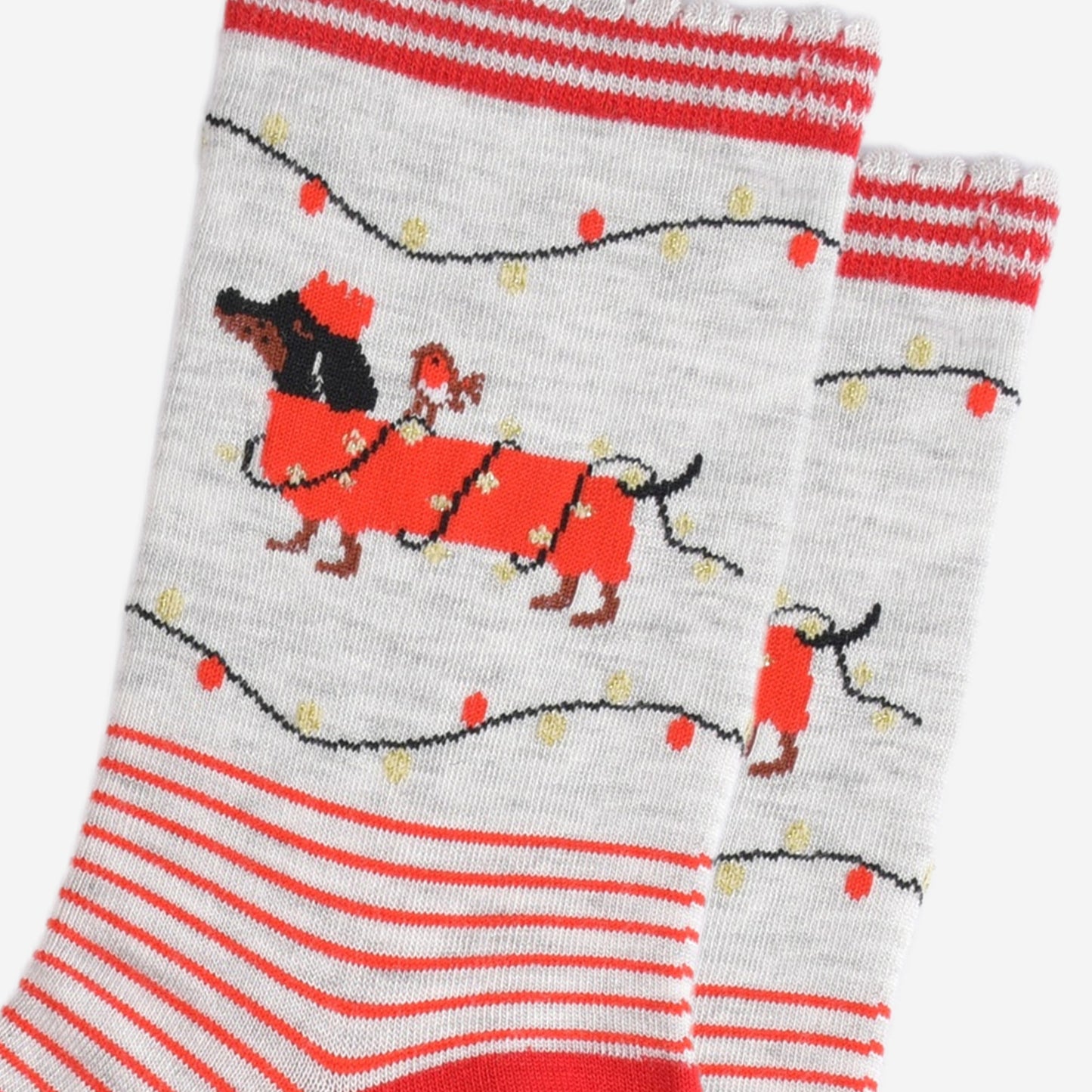 close up of the party lights and sausage dog design on the ankle of the socks, the dog is black and is wearing a red festive coat wrapped in gold party lights, there is a robin bird sitting on the dogs back. the dog is also wearing a red crown party hat and there are party lights above and below the dog in red and gold