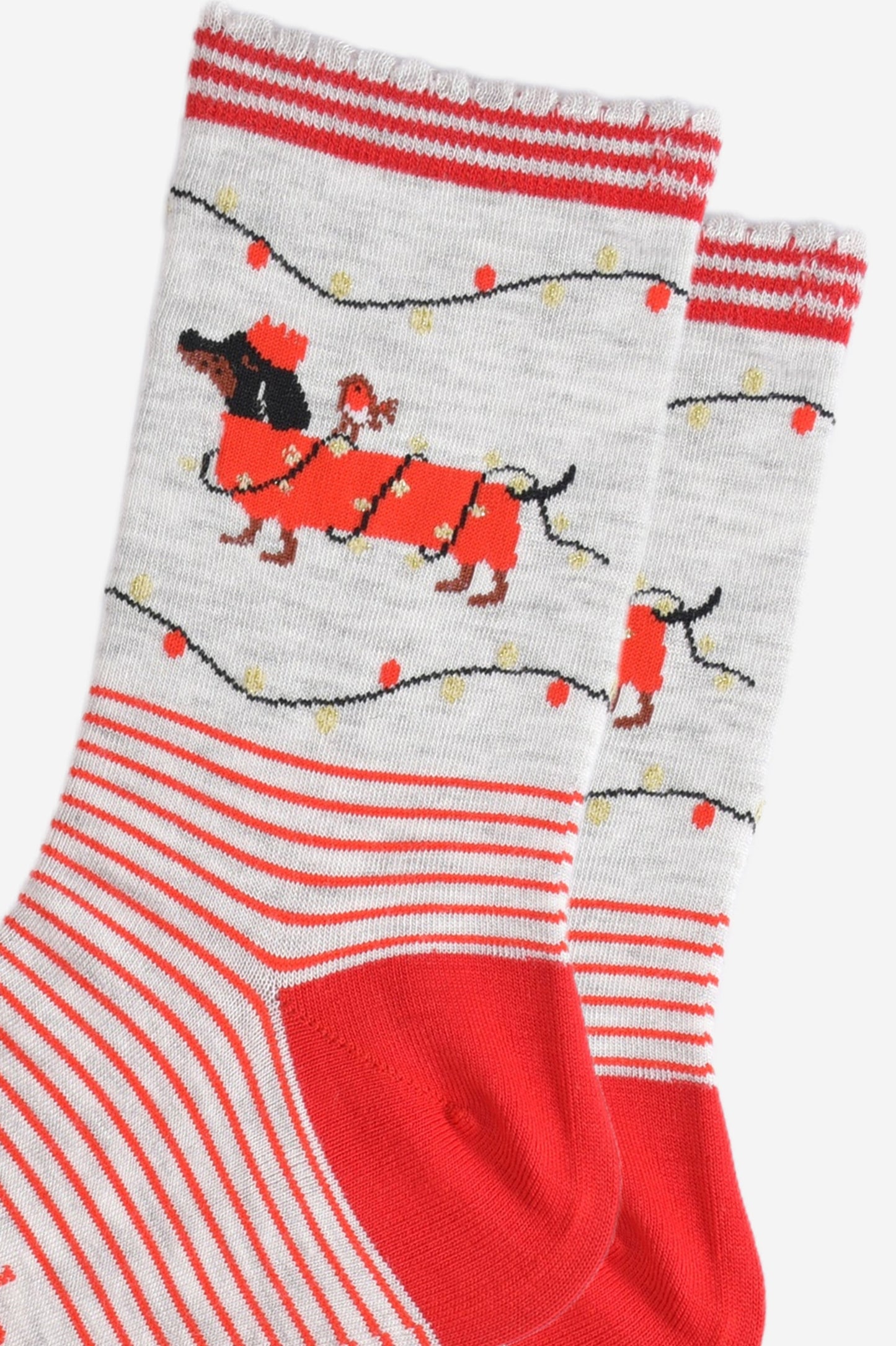 close up of the party lights and sausage dog design on the ankle of the socks, the dog is black and is wearing a red festive coat wrapped in gold party lights, there is a robin bird sitting on the dogs back. the dog is also wearing a red crown party hat and there are party lights above and below the dog in red and gold