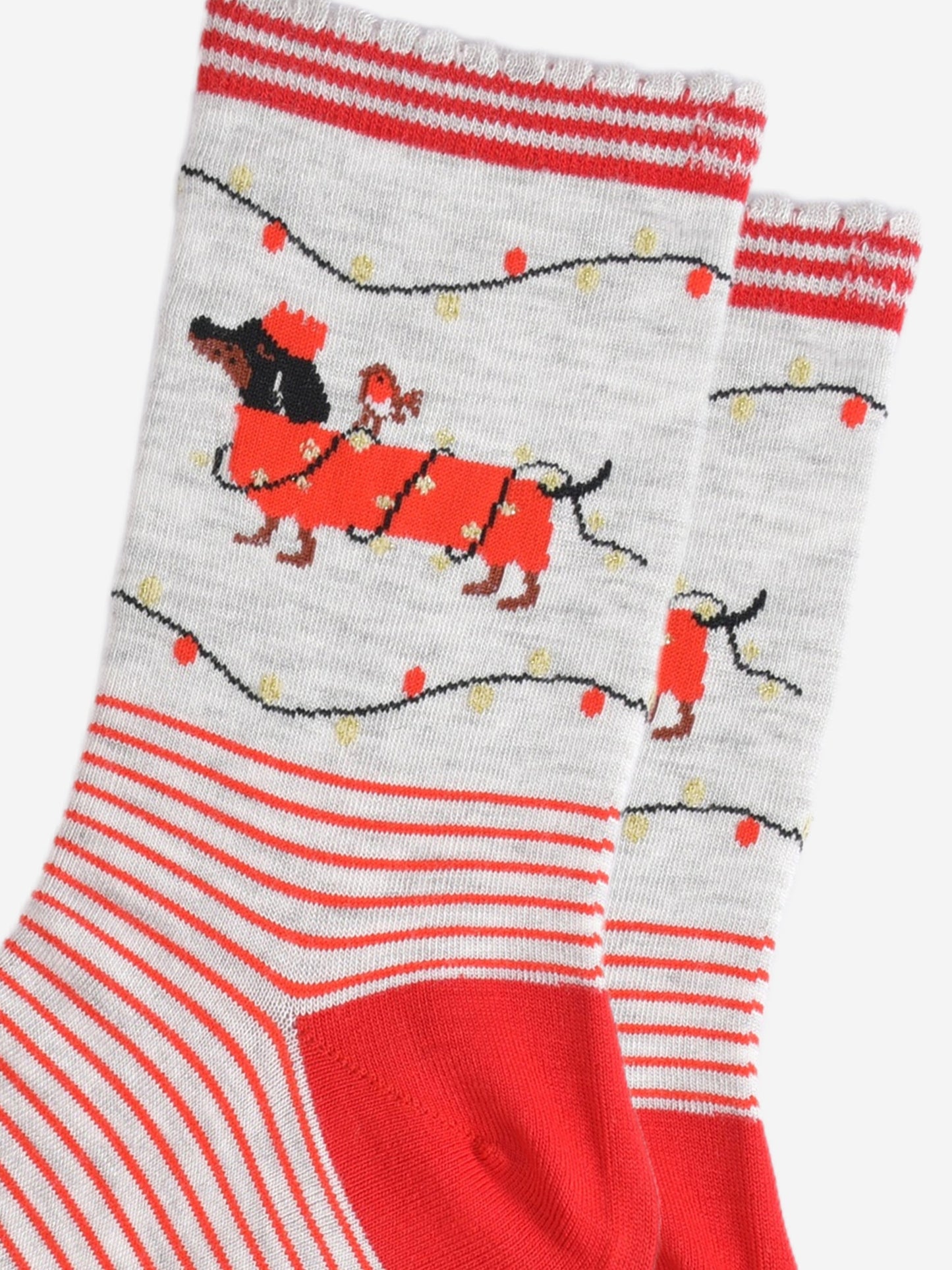 close up of the party lights and sausage dog design on the ankle of the socks, the dog is black and is wearing a red festive coat wrapped in gold party lights, there is a robin bird sitting on the dogs back. the dog is also wearing a red crown party hat and there are party lights above and below the dog in red and gold