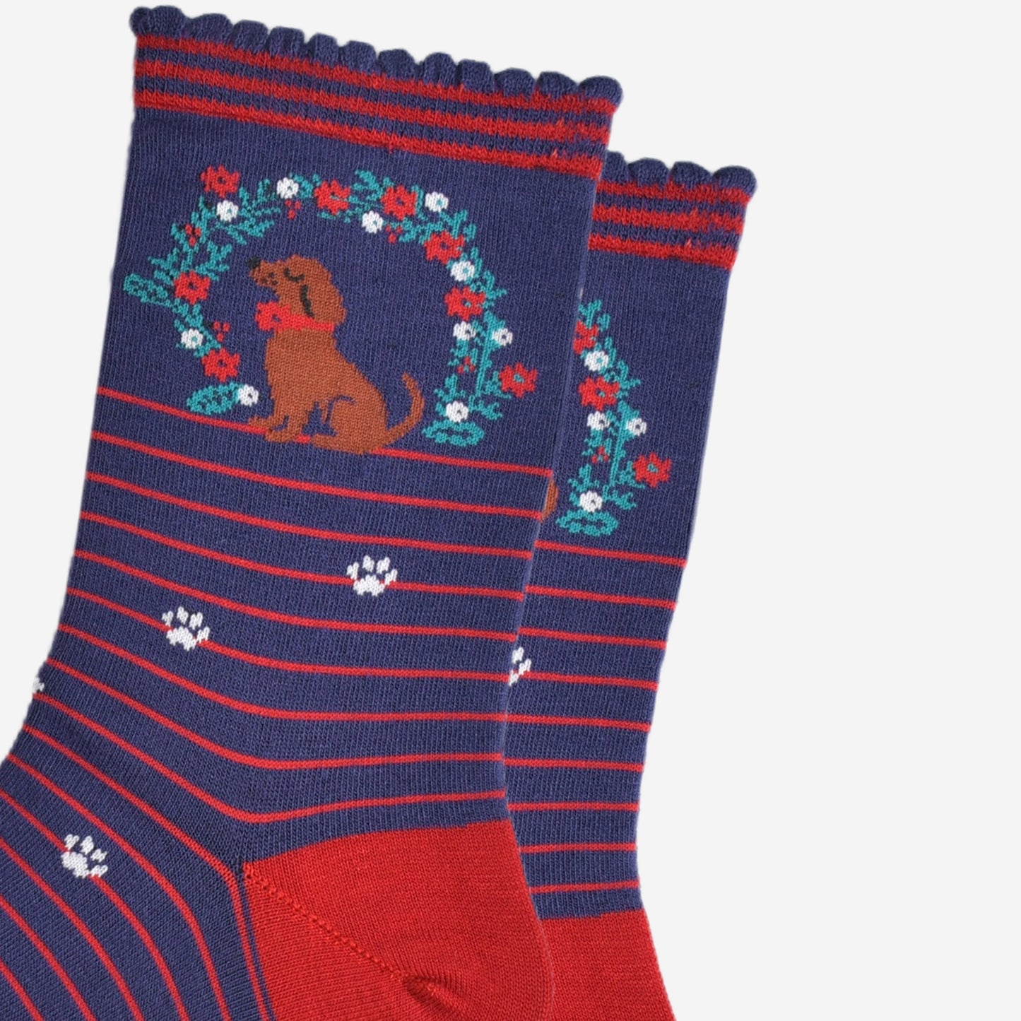 close up of the sausage dog and floral wreath on the ankle of the bamboo socks, the wreath is green with red and white flowers, the dog is brown and is wearing a red collar.