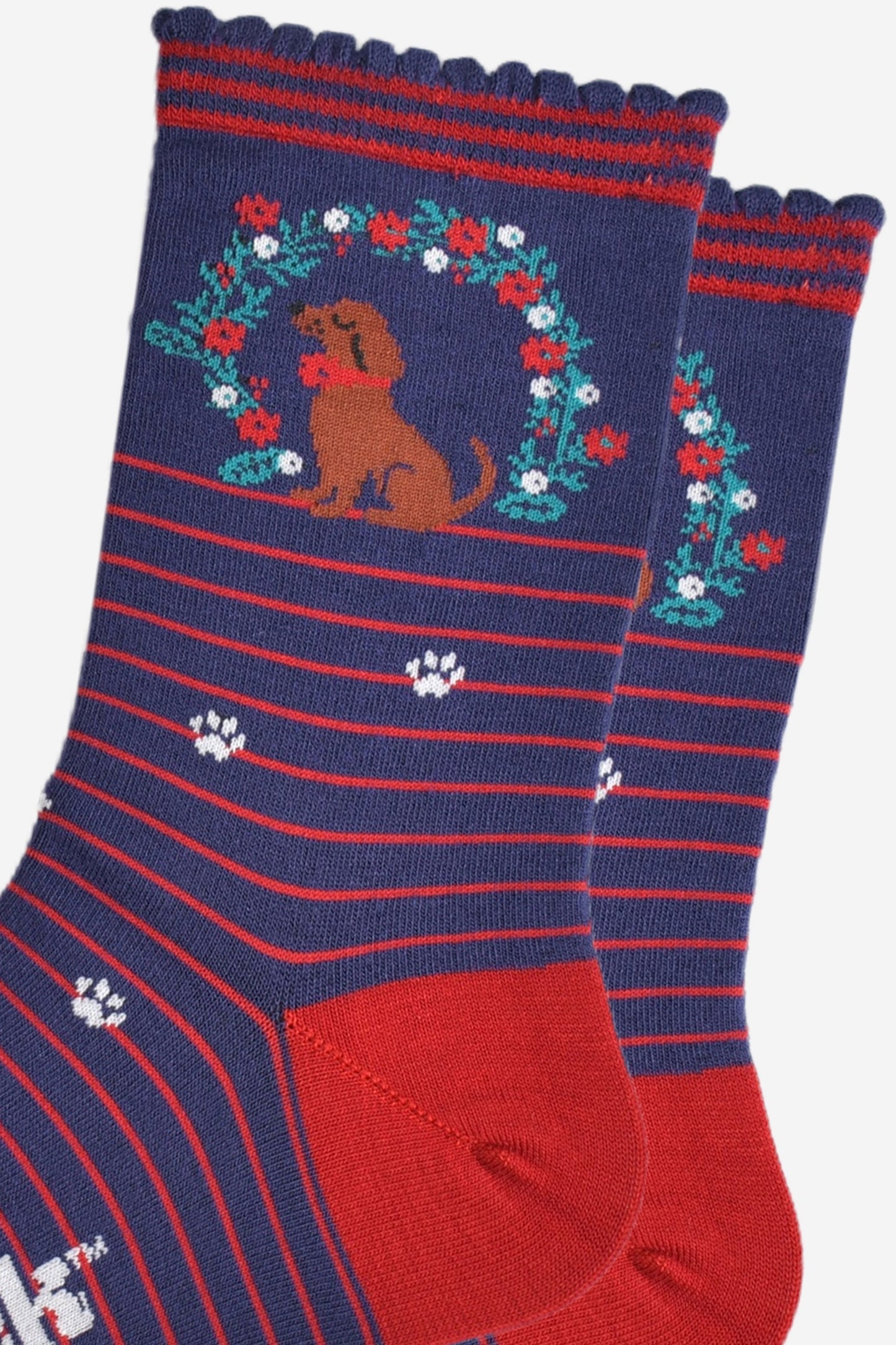 close up of the sausage dog and floral wreath on the ankle of the bamboo socks, the wreath is green with red and white flowers, the dog is brown and is wearing a red collar.