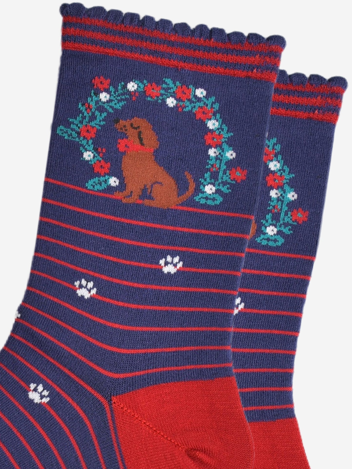 close up of the sausage dog and floral wreath on the ankle of the bamboo socks, the wreath is green with red and white flowers, the dog is brown and is wearing a red collar.