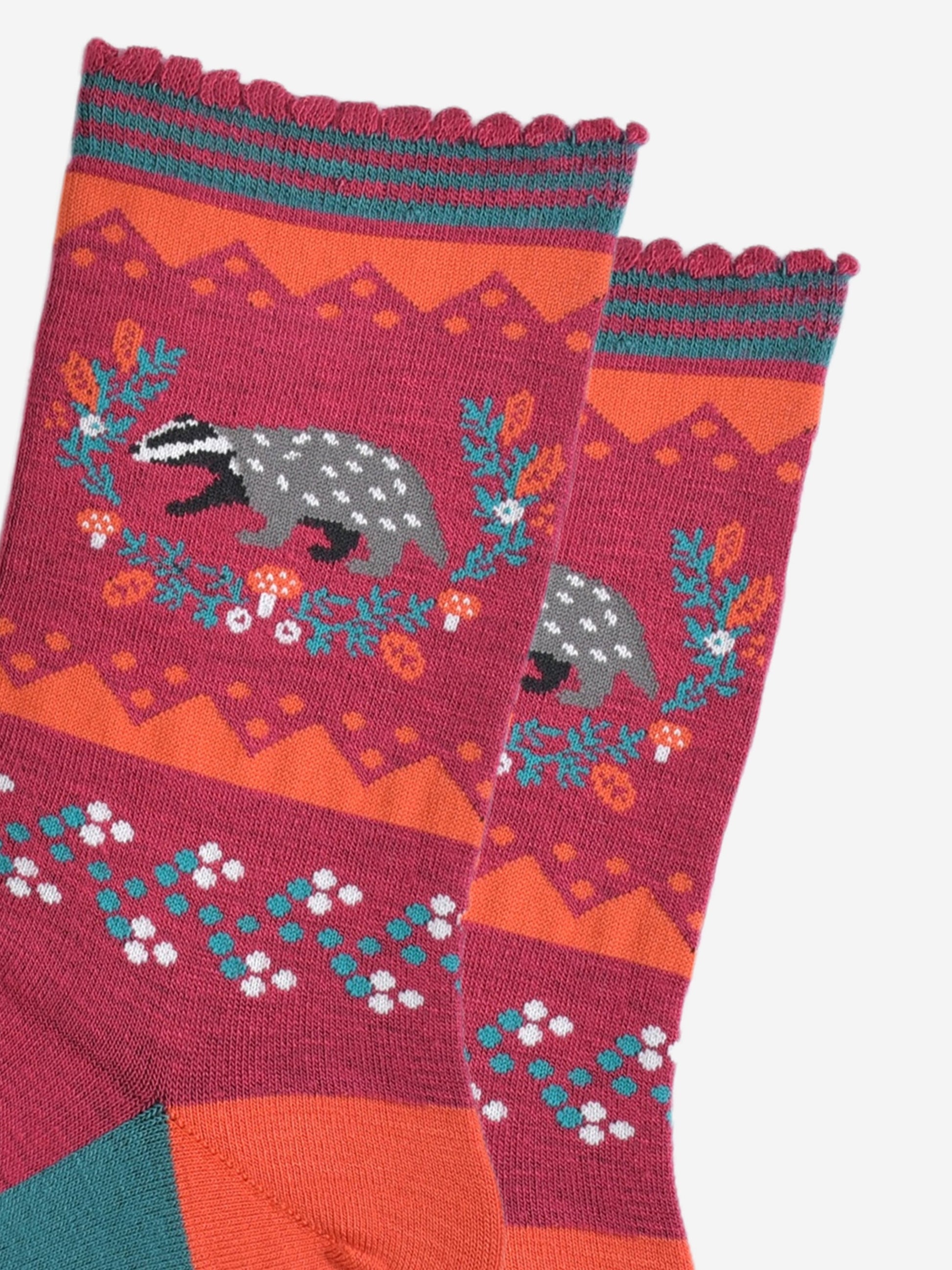 close up of the badger and wreath on the ankle of the socks, the badger is grey and black and the wreath is freen with red toadstool and autumn leaf accents