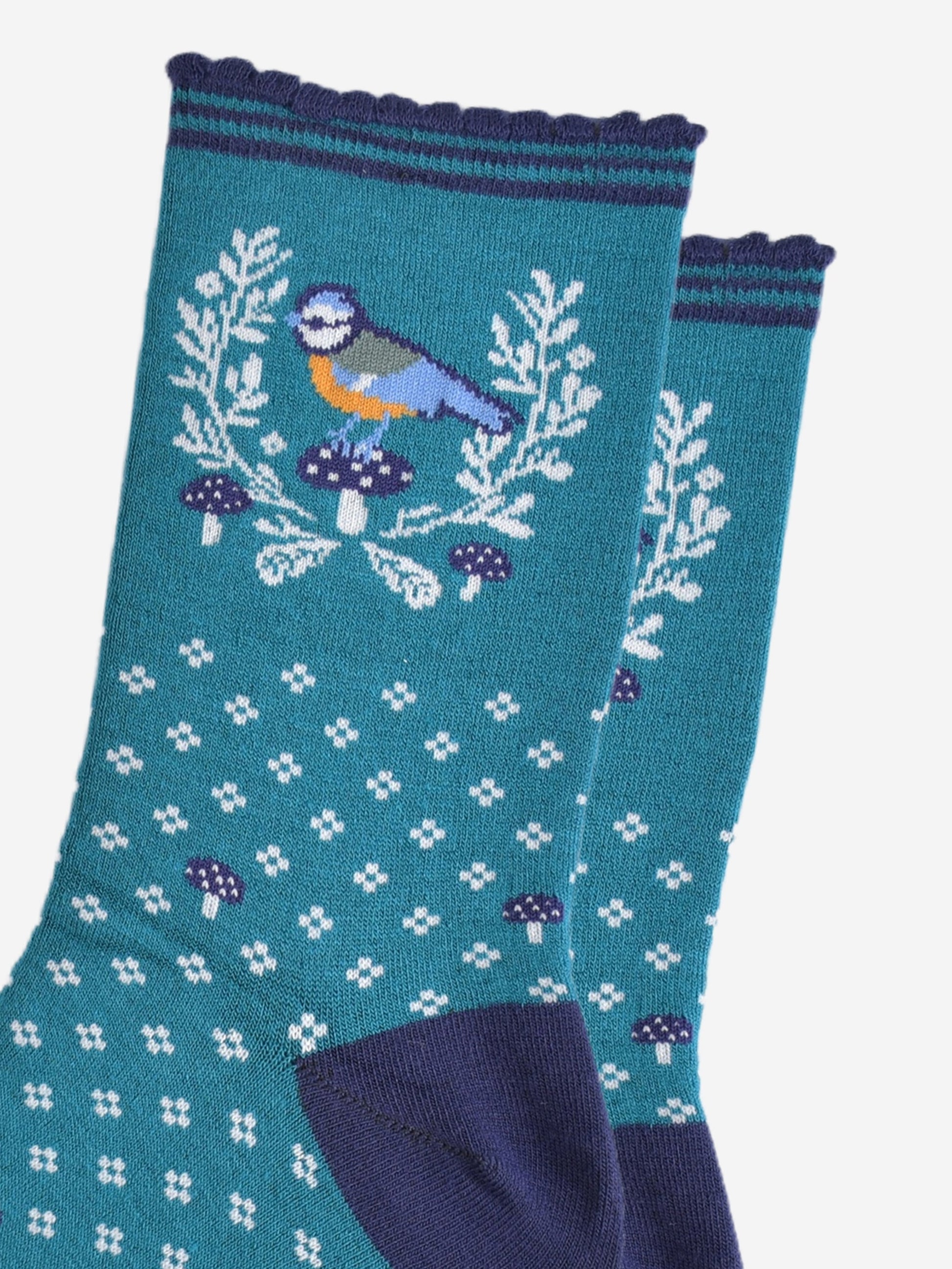 close up of the blue tit bird motif on the ankle of the socks, the bird is perched on a blue toadstool and surrounded by a white horseshoe shaped wreath