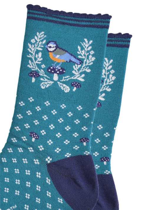 close up of the blue tit bird motif on the ankle of the socks, the bird is perched on a blue toadstool and surrounded by a white horseshoe shaped wreath