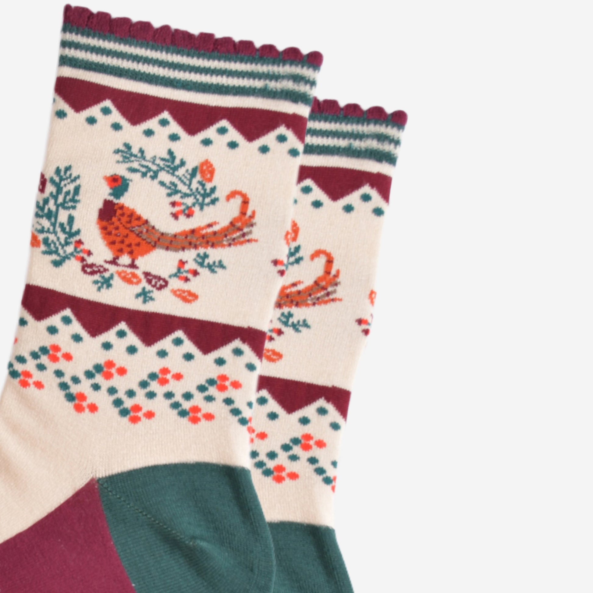 close up of the woodland pheasant and autumnal wreath on the ankle of the socks, the pheasants are stranding in the middle of a green horseshoe shaped wreath, there are orange and red fallen leaves scattered around